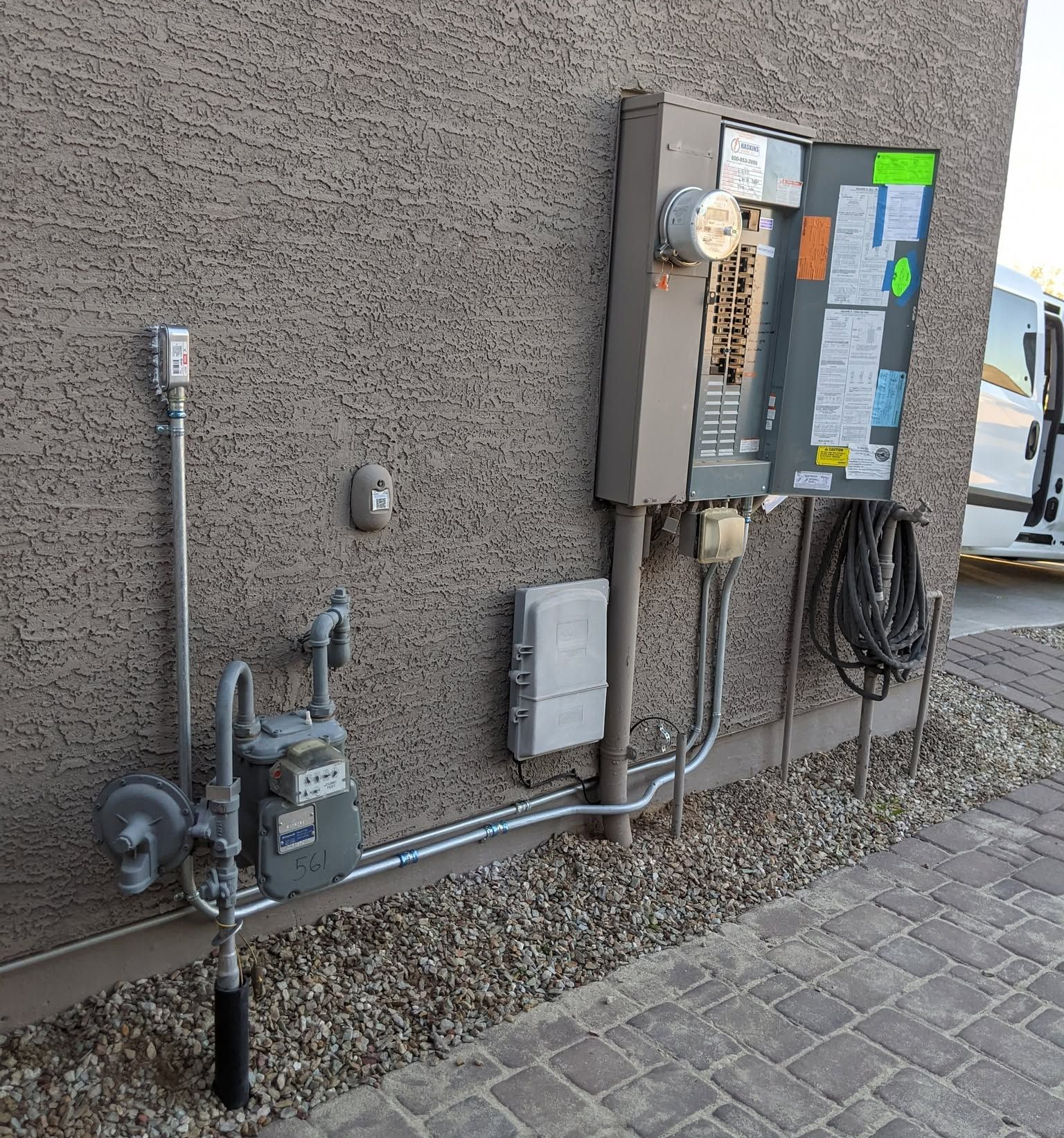 Utility meters and electrical boxes mounted on a stucco wall beside a paved walkway.