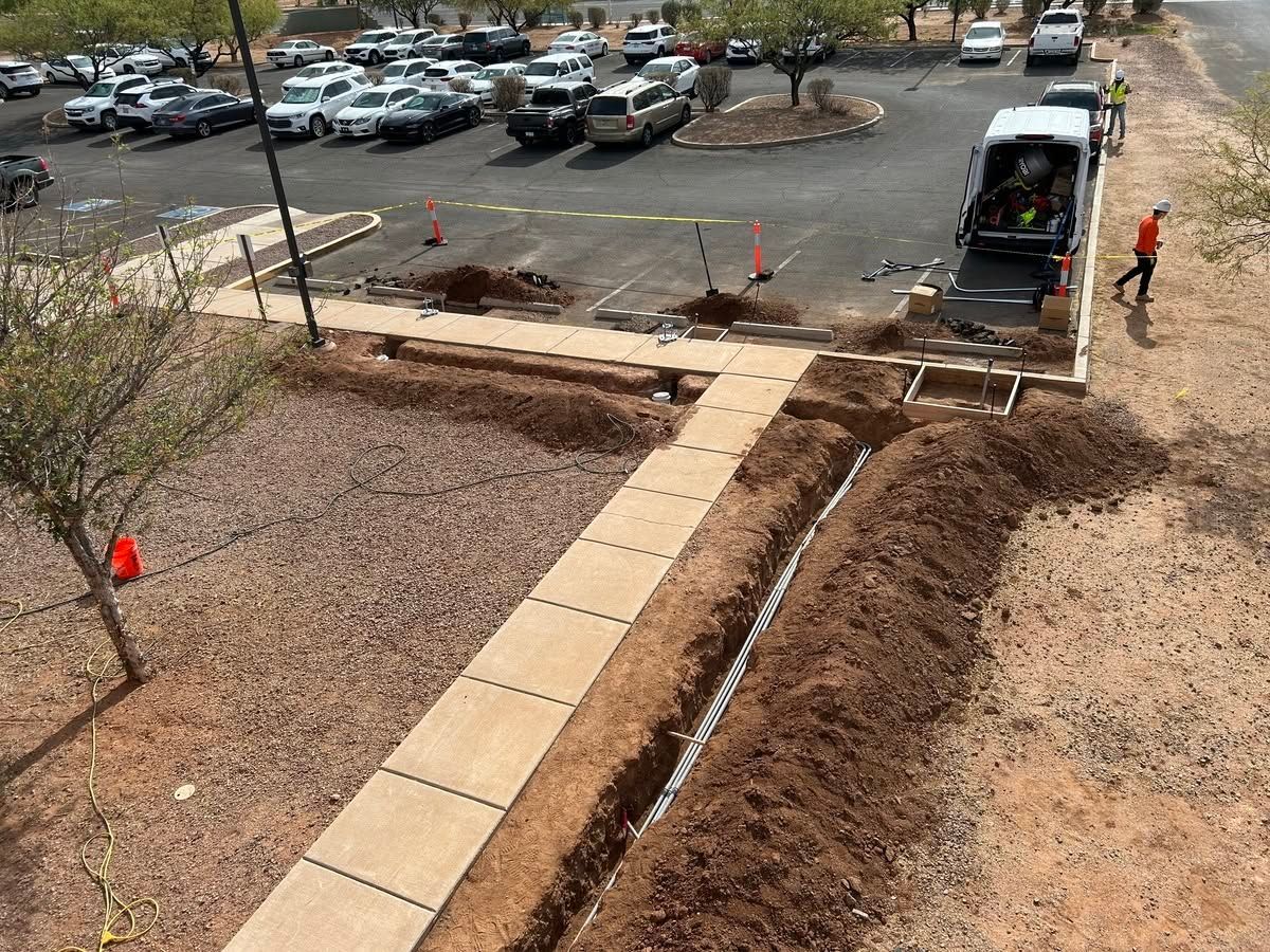 Construction workers building a sidewalk ramp beside a parking lot, with concrete paths and orange cones