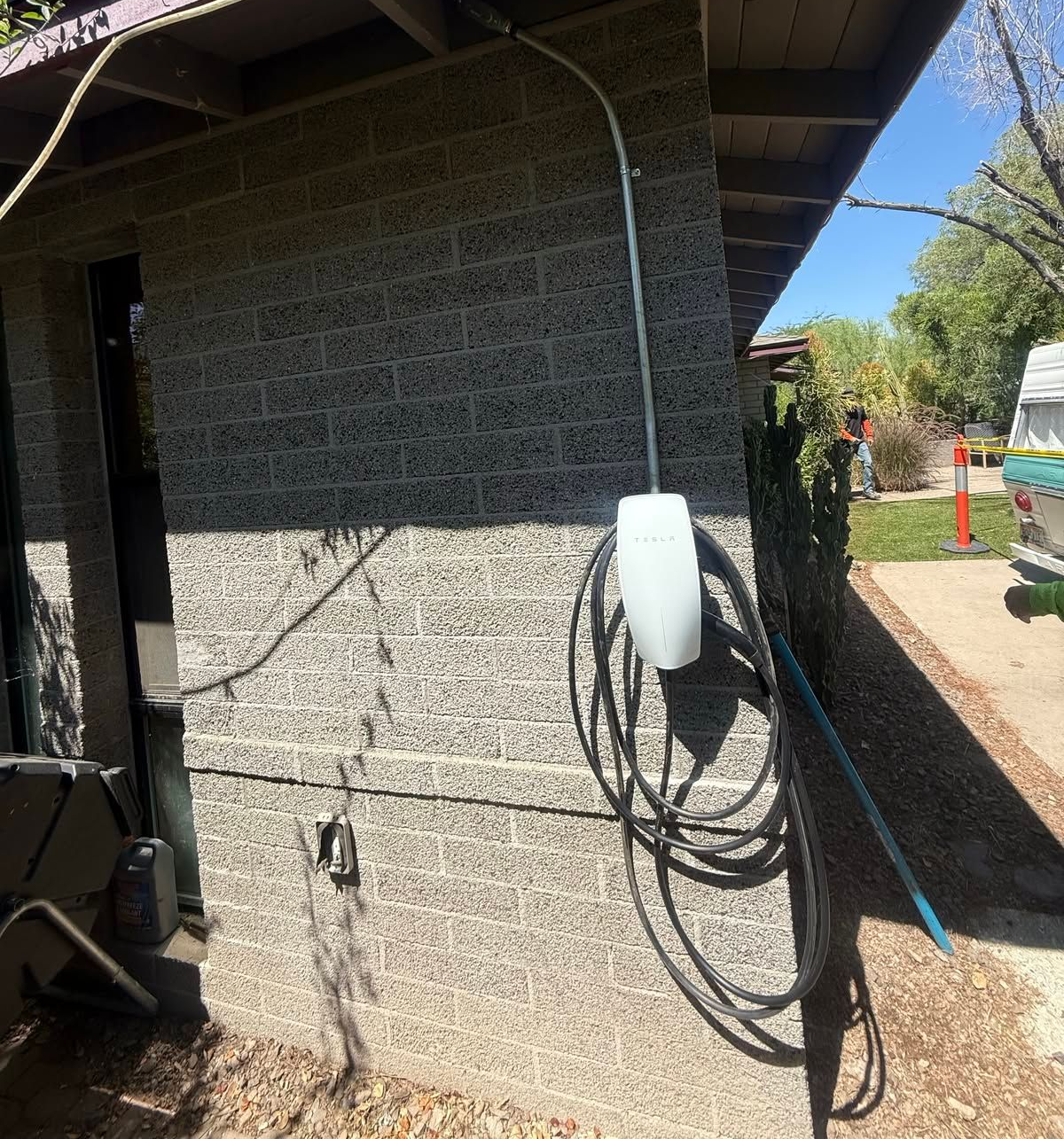 Outdoor utility wall with mounted white charger box and coiled cable beside a house driveway