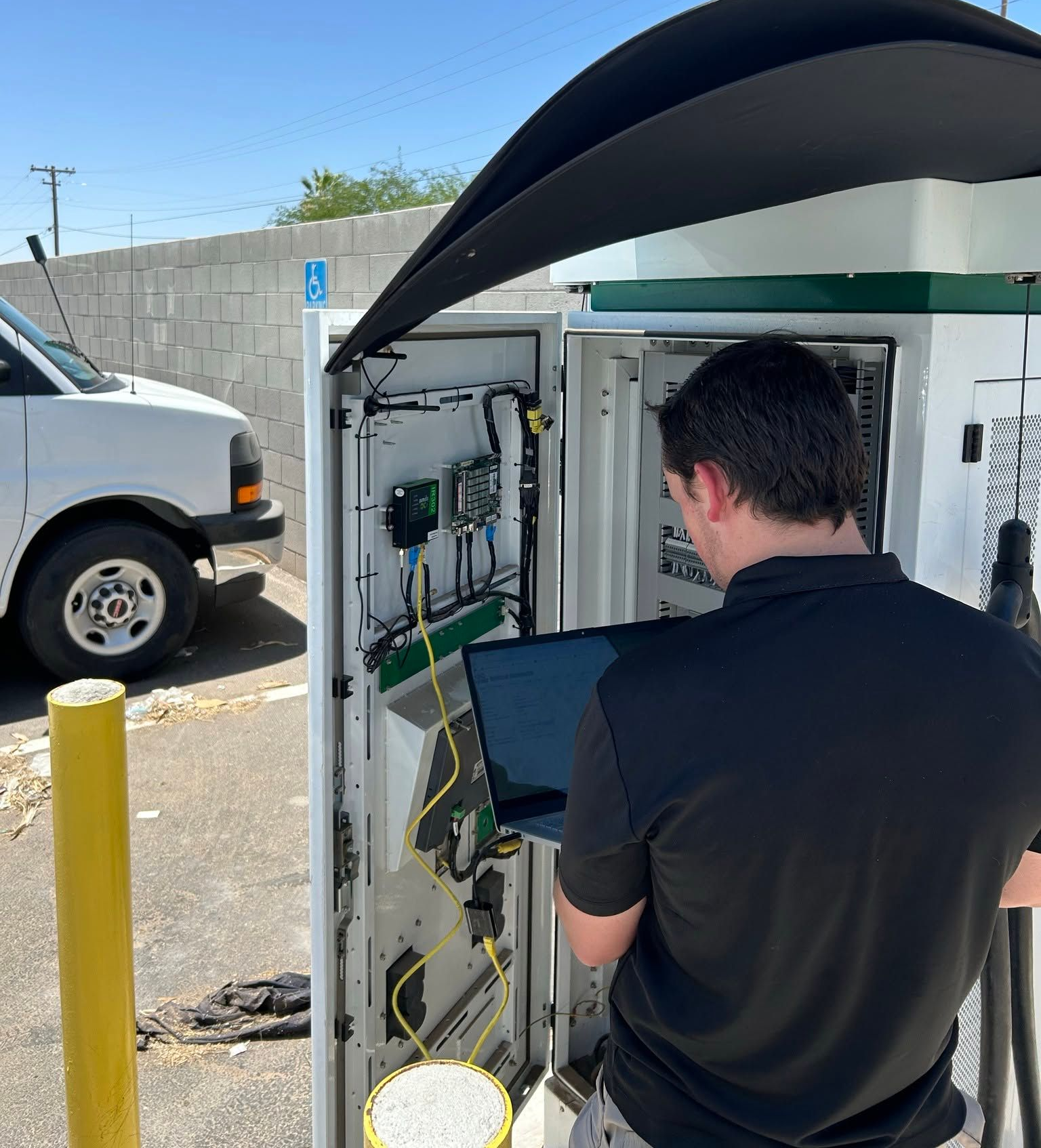Technician inspecting open utility cabinet outdoors beside a van in a parking lot