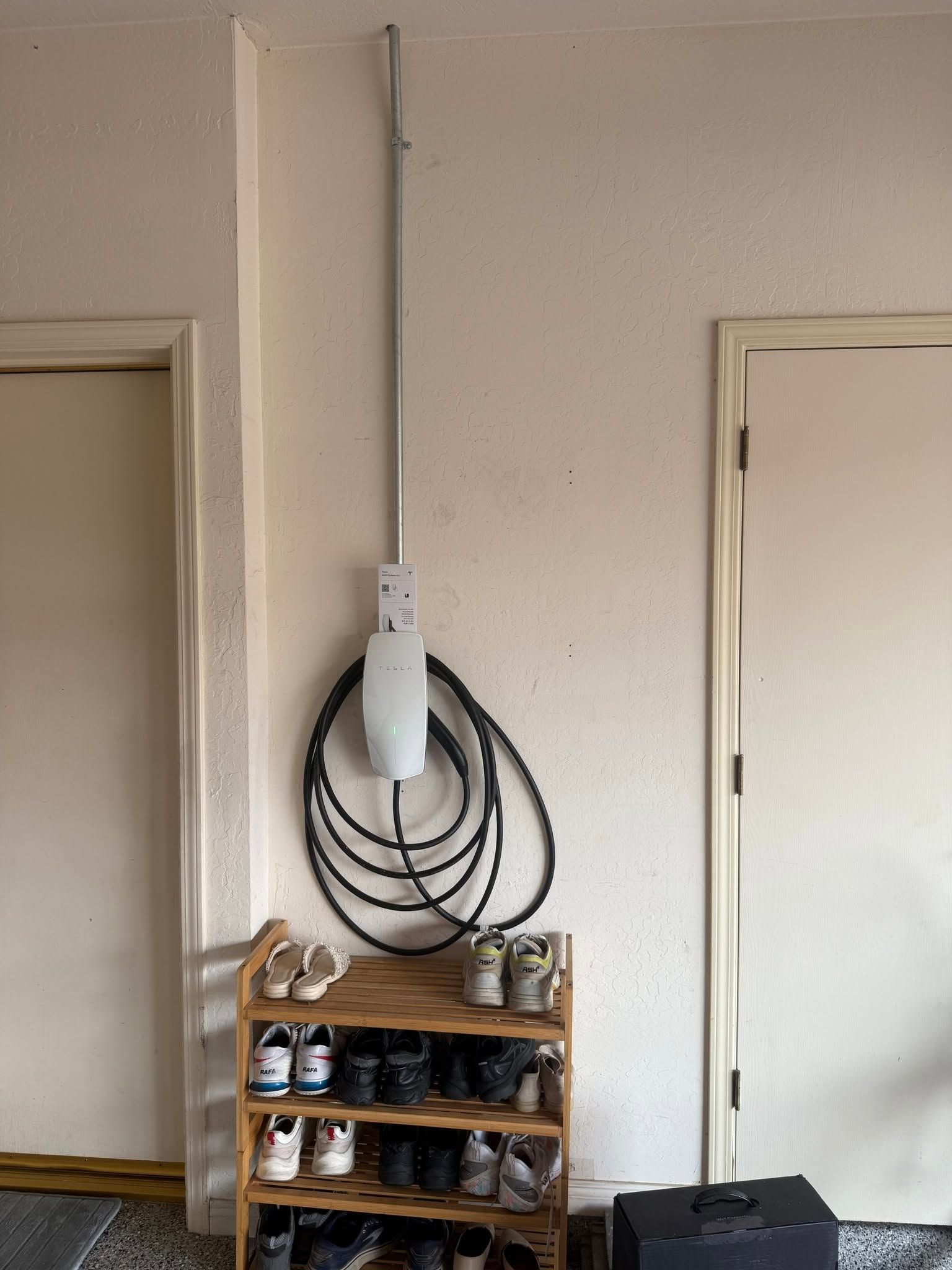 Coiled black cable on wall above a shoe rack between two doorways in a beige room