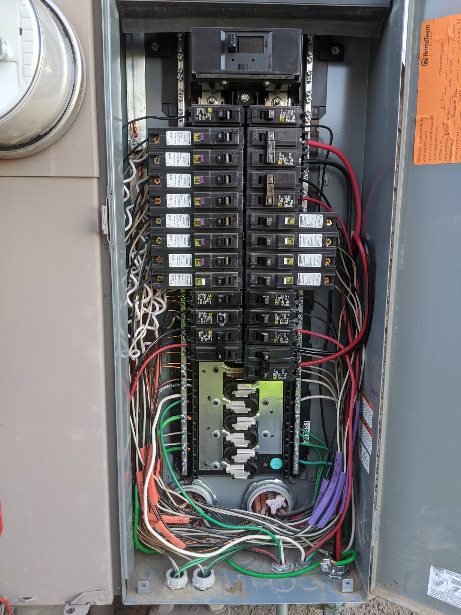 Open electrical breaker panel with rows of switches and colored wiring inside a metal cabinet.