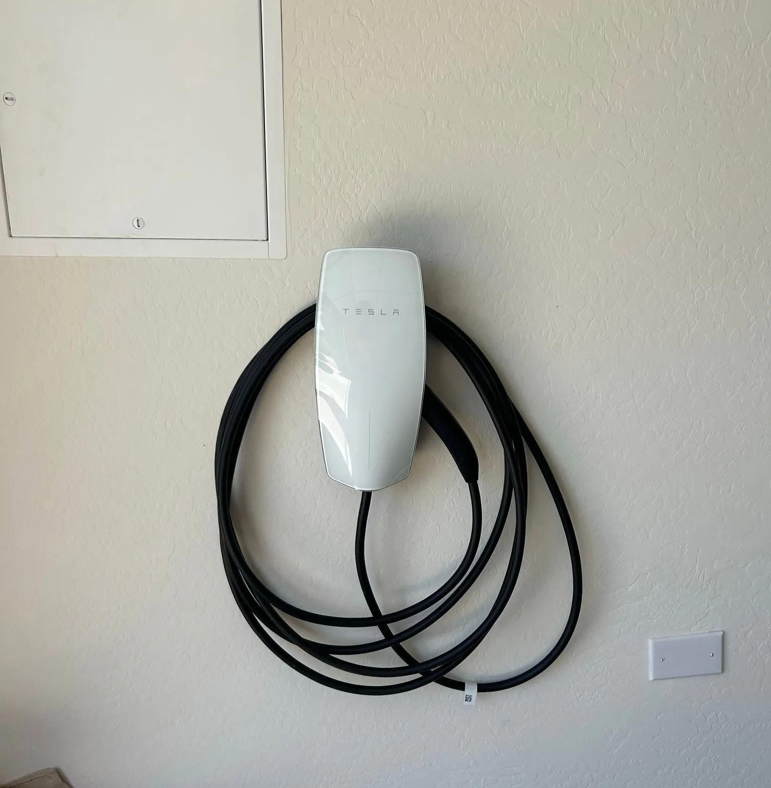 Coiled black cable hanging from a white wall-mounted device on a beige wall