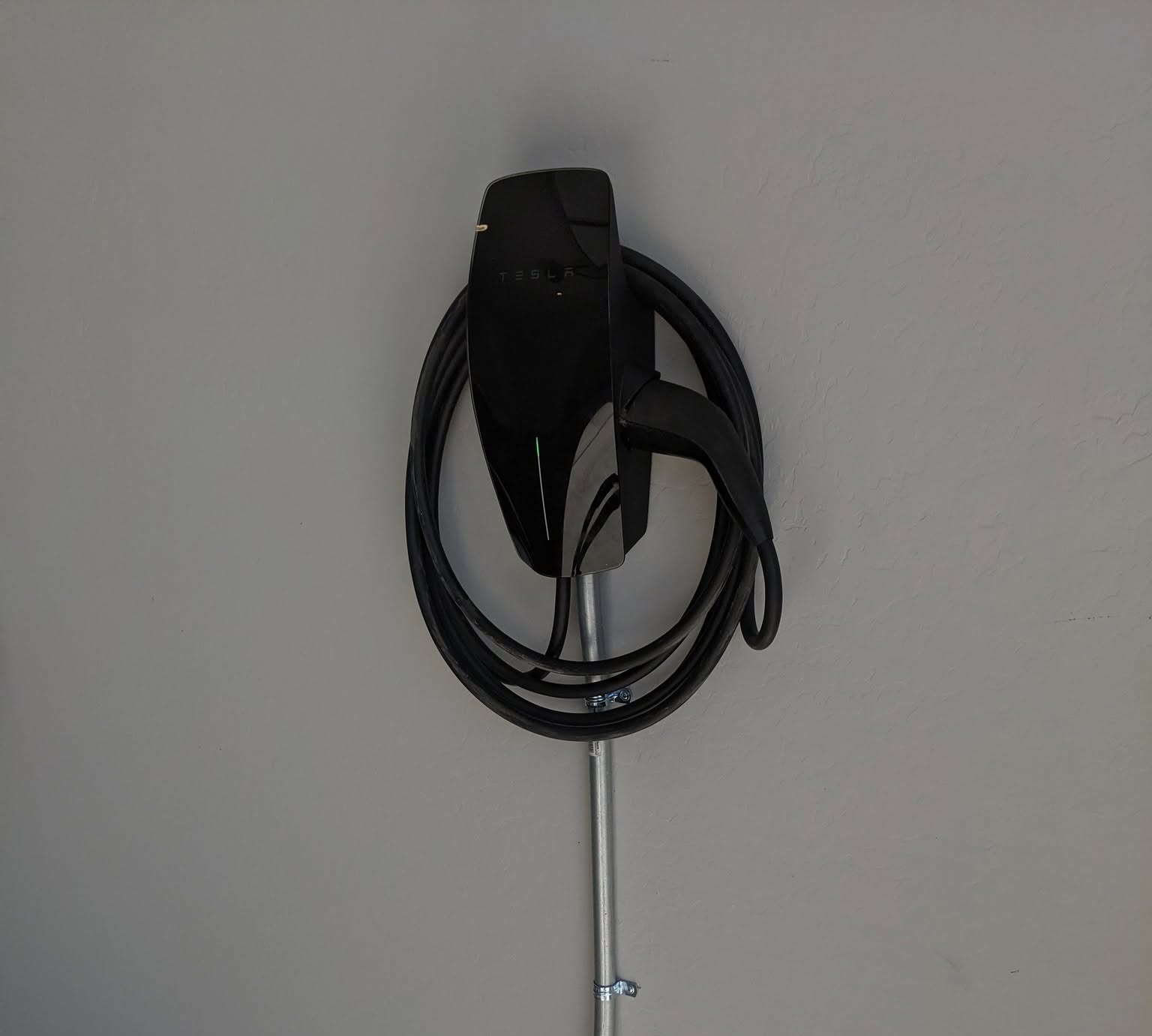 Black EV charging cable coiled on a wall-mounted holder against a light gray background