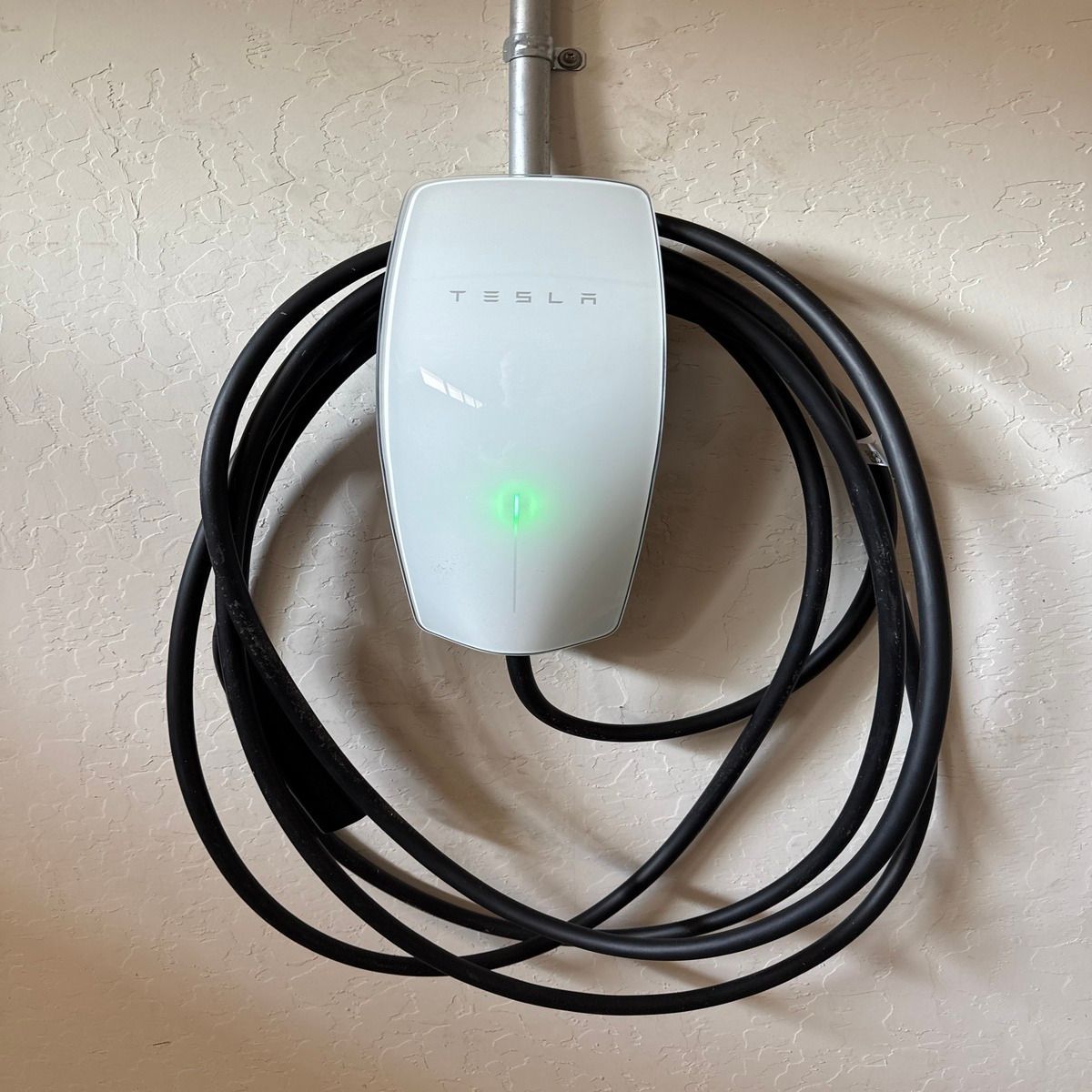 White wall-mounted charger with a green light and coiled black cable
