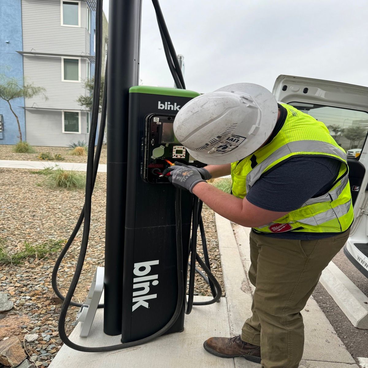 Worker in reflective vest servicing a Blink EV charging station outdoors