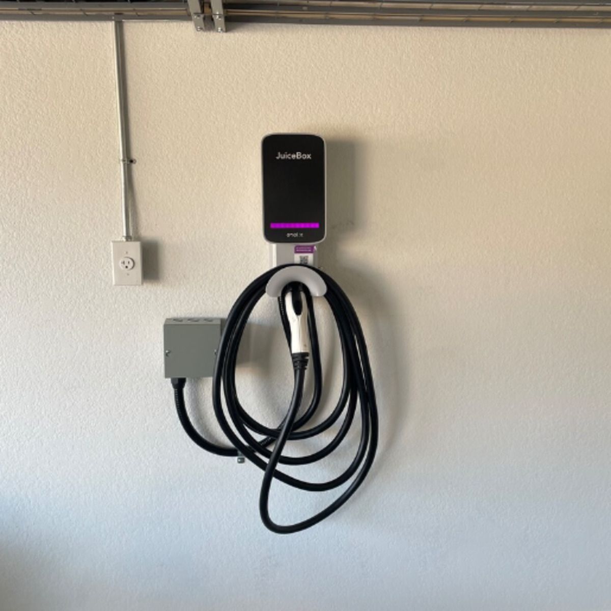 Wall-mounted electric vehicle charger with coiled black cable and purple indicator light on a beige wall