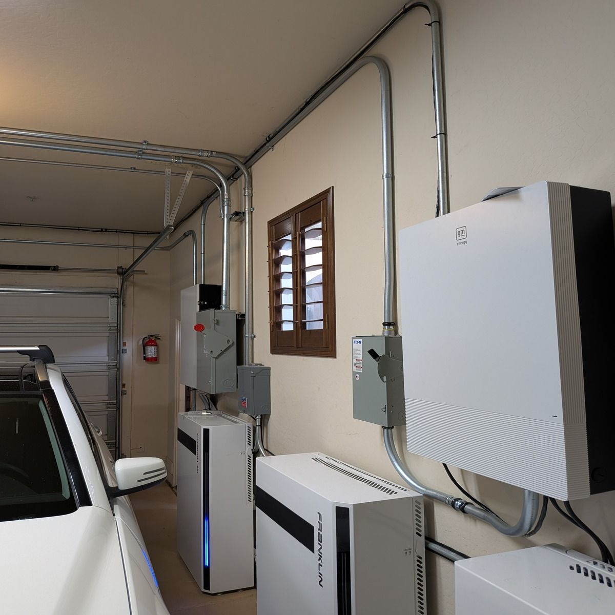 Garage wall with electrical panels, conduit, and a car parked inside.