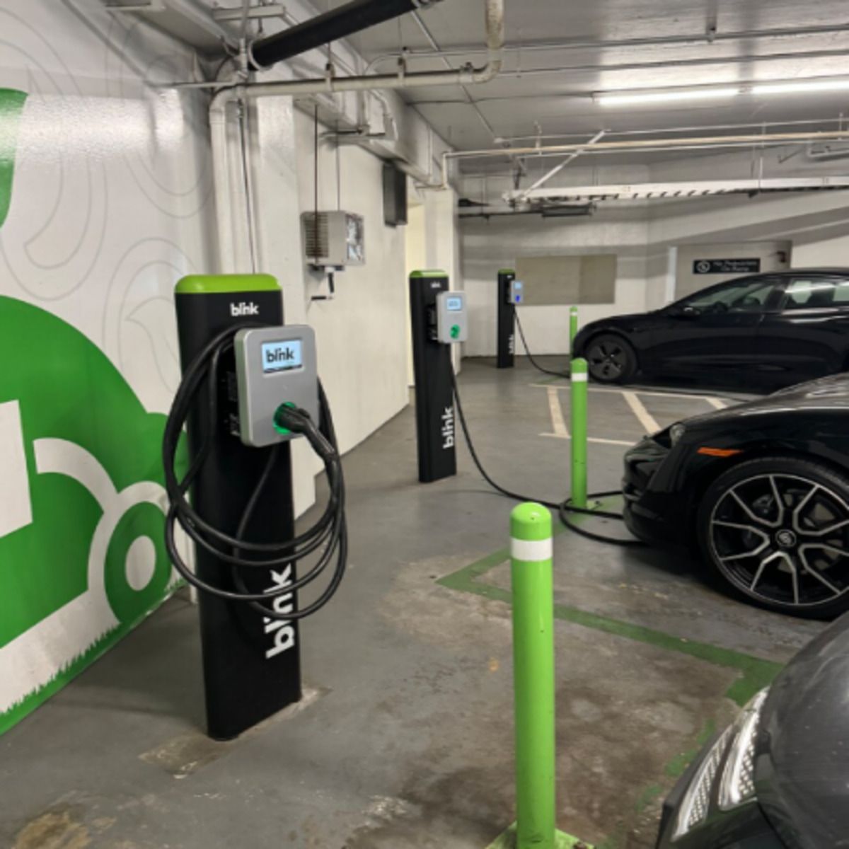 Electric vehicle charging station in a garage, with black and green chargers beside parked cars.