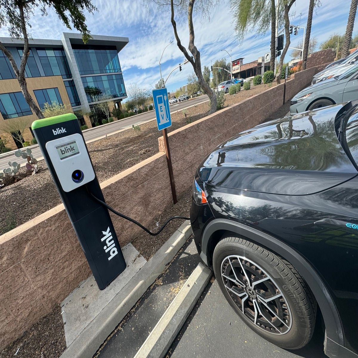 Electric vehicle charging station beside a parked black car in a lot outdoors