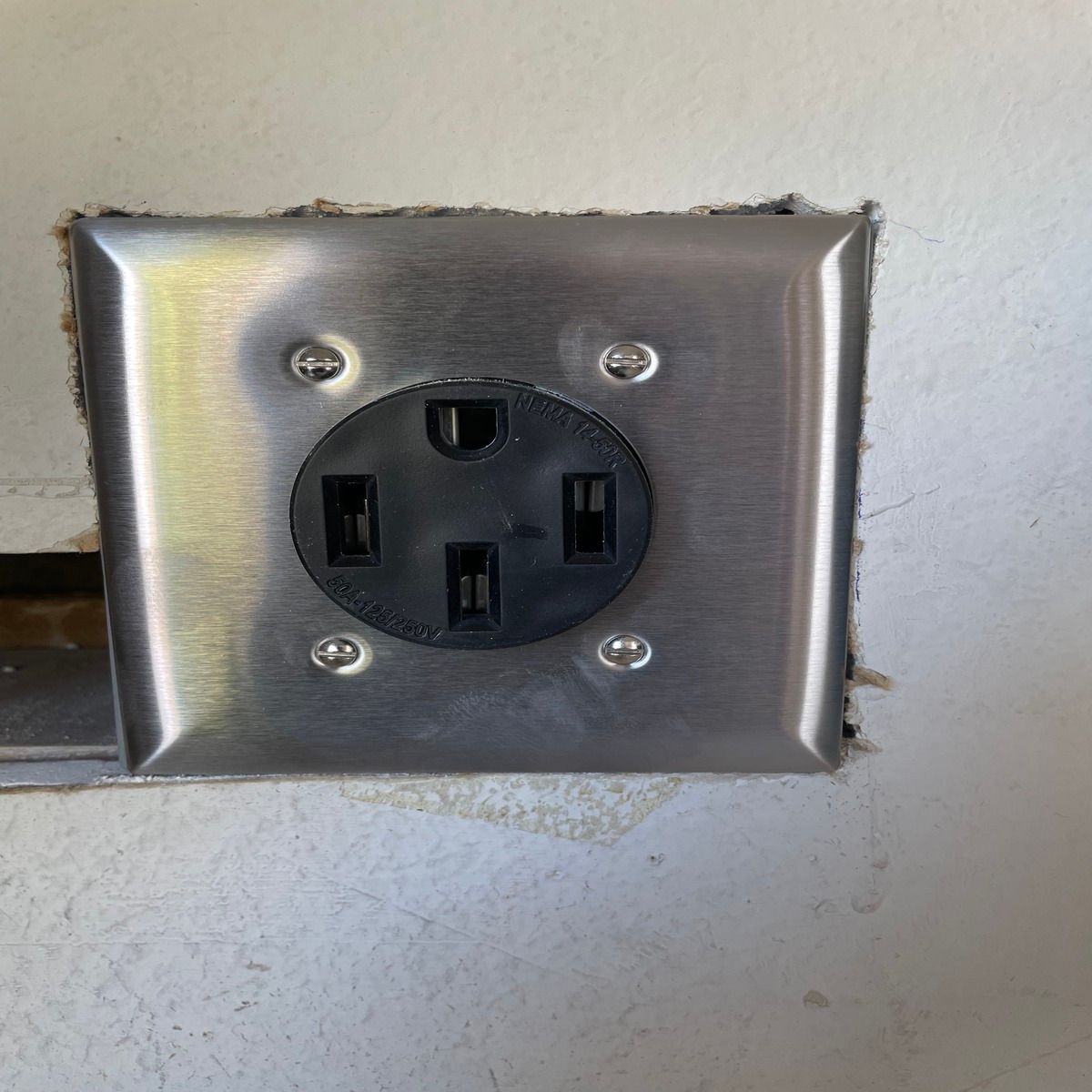 Stainless steel wall plate with a black electrical outlet on a light-colored wall.