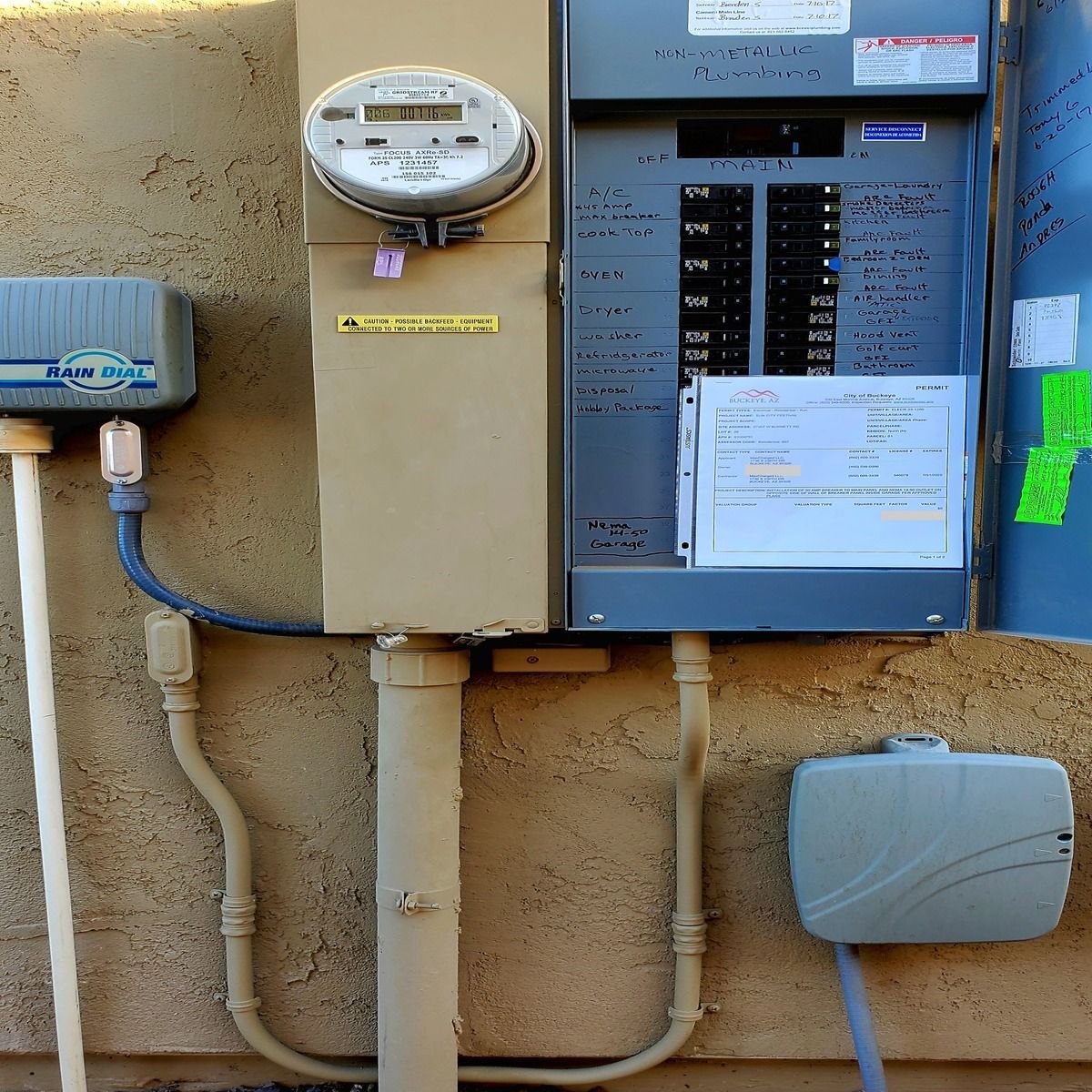 Electrical meter and breaker panel mounted on a tan exterior wall with conduit and utility boxes.