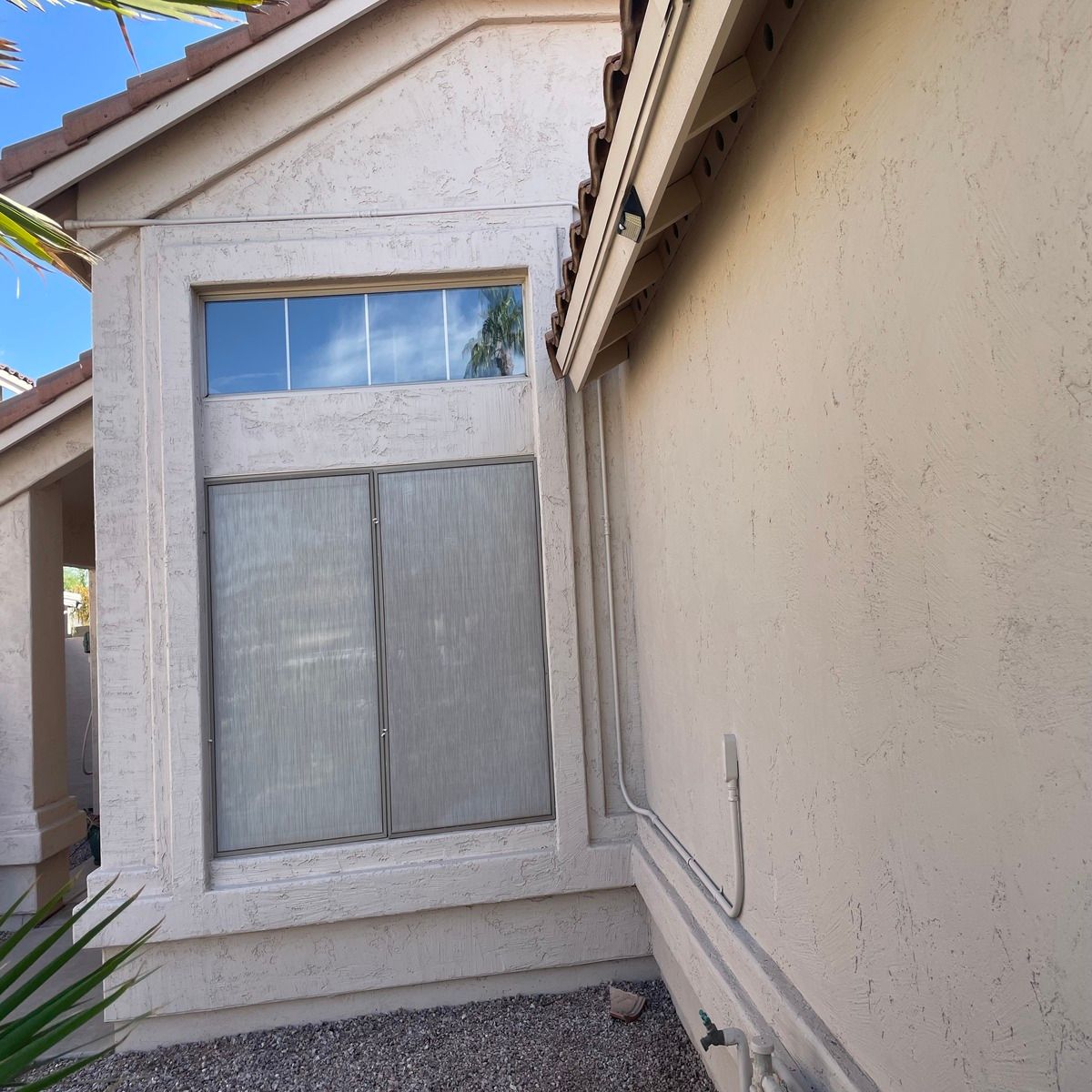 Backyard view of a house window with white blinds and stucco walls.