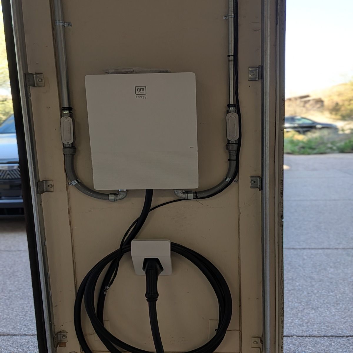 Wall-mounted electrical box with conduit and coiled black cable beside a doorway outdoors