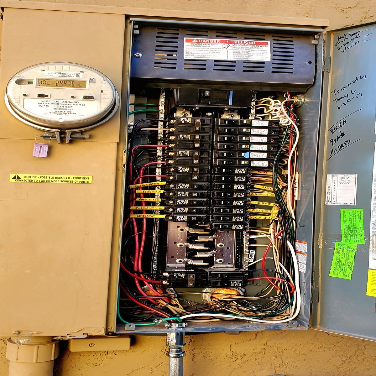 Open electrical breaker panel with exposed wiring and meters on a beige wall