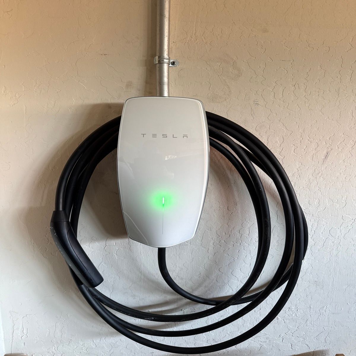 Coiled black charging cable hanging on a wall-mounted EV charger in a garage.