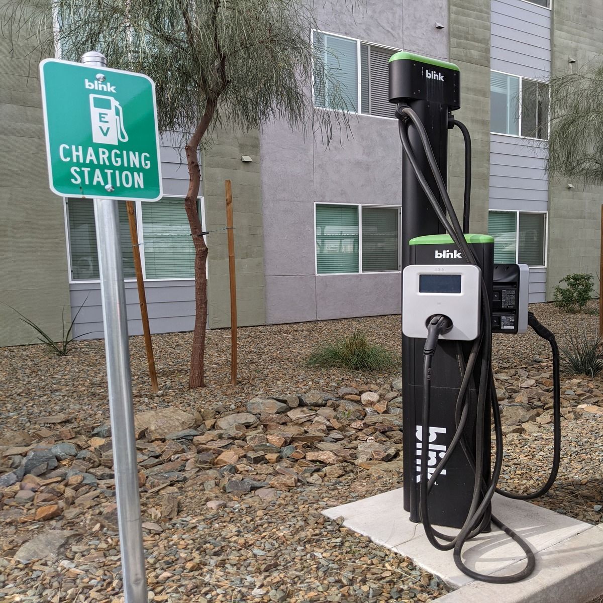 EV charging station with black charger beside a green parking sign outside an apartment building
