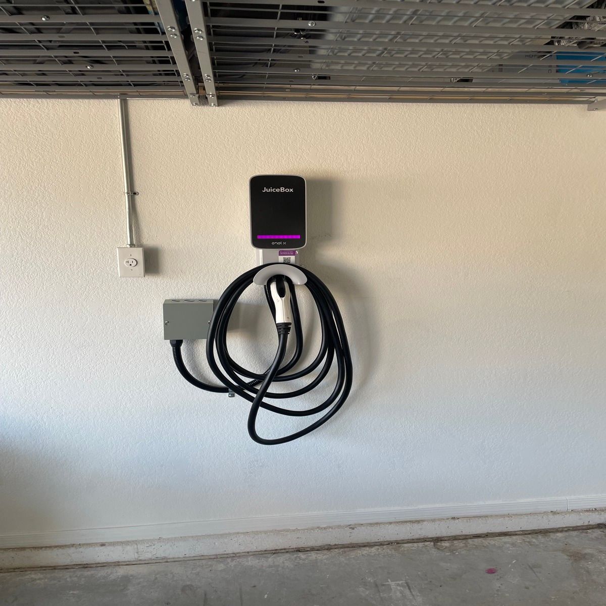 Wall-mounted EV charging station with coiled black cable in a garage.