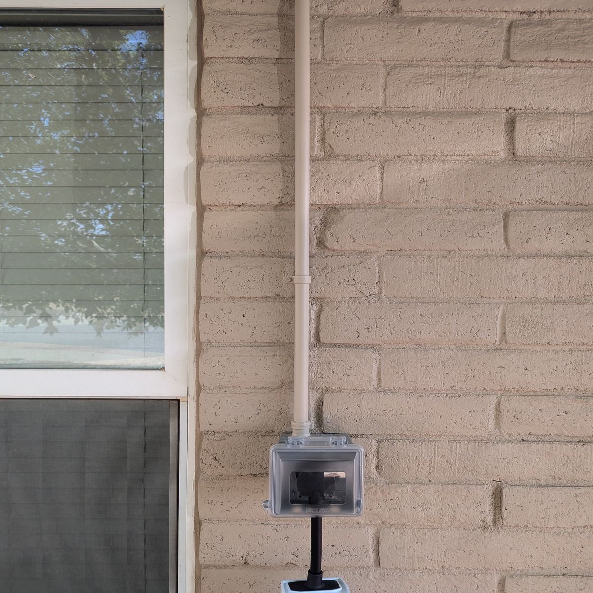 Exterior brick wall with window, white conduit, and electrical meter box.