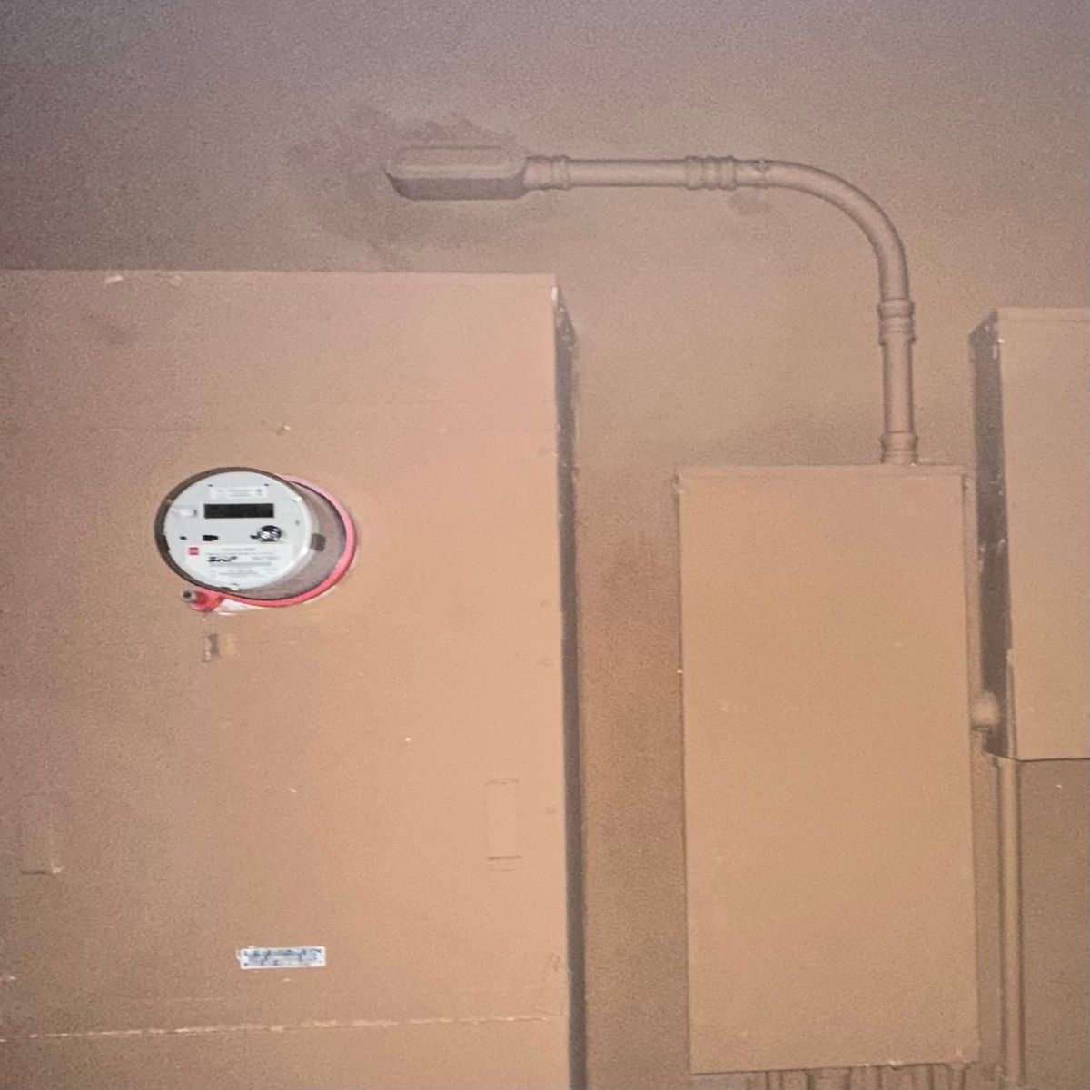 Wall-mounted meter and beige utility boxes with exposed conduit in a dim industrial room
