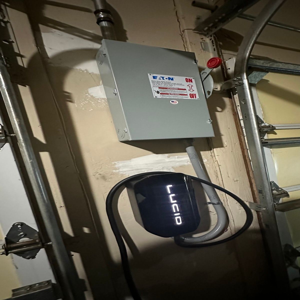 Basement utility area with gray electrical panel and black Lucid device mounted near exposed pipes.