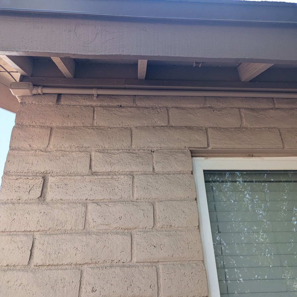 Close-up of a beige stucco exterior wall with roof eaves and the top corner of a window