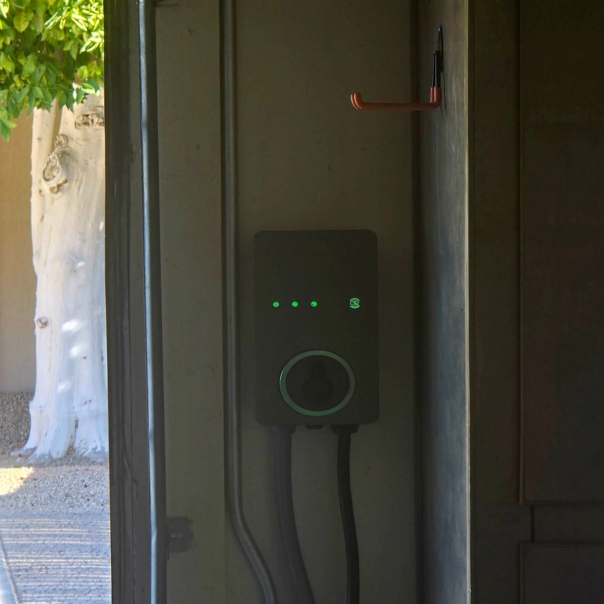 Wall-mounted EV charger with green lights in a shaded doorway