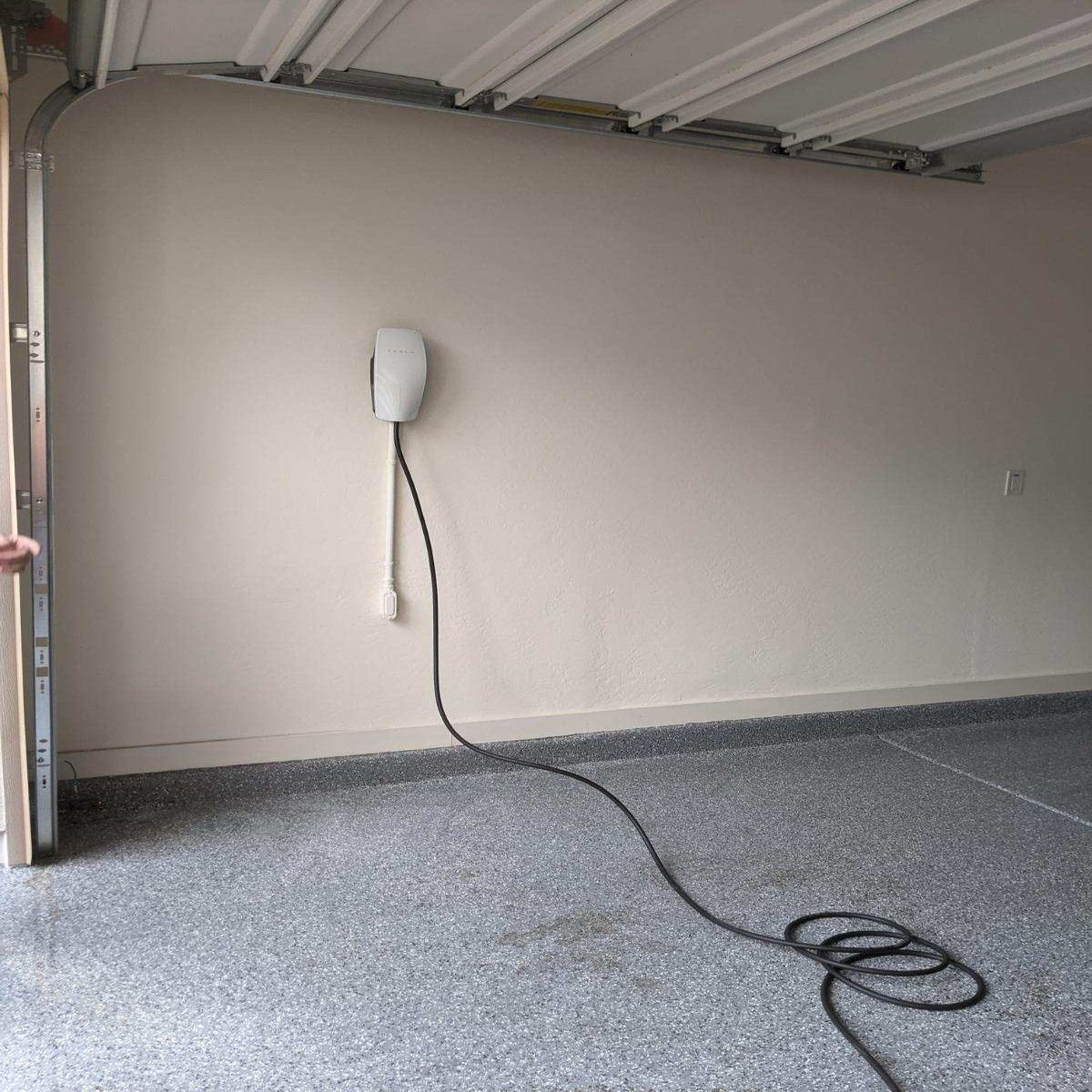 Empty garage wall with a mounted white charger and a black cord on the floor