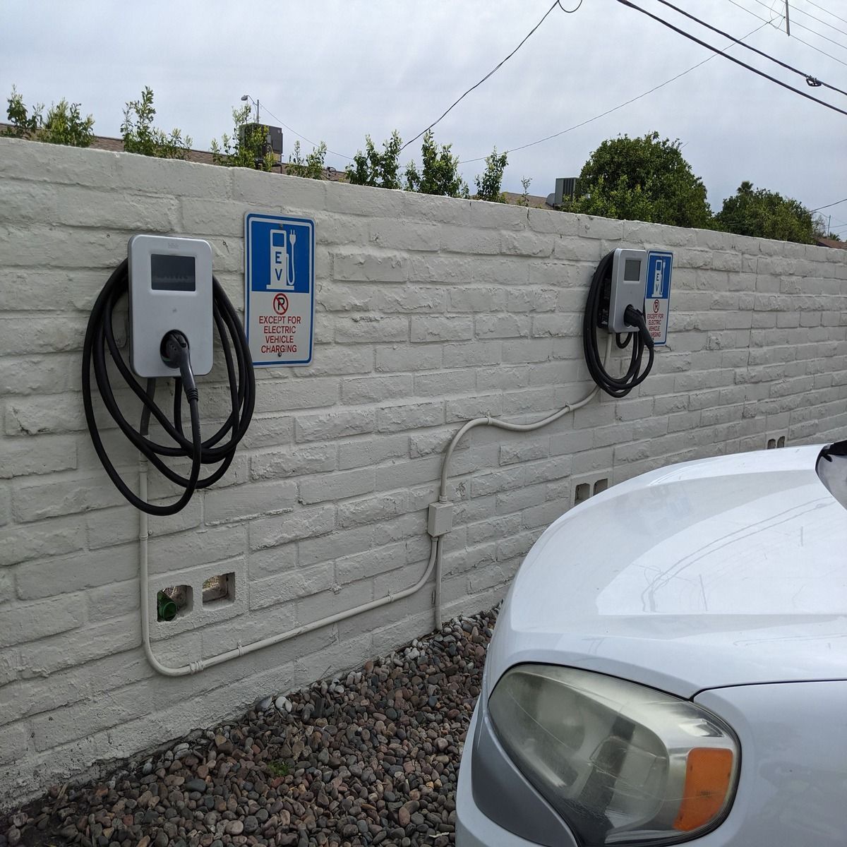 Two wall-mounted EV charging stations beside a parked car in a gravel lot.