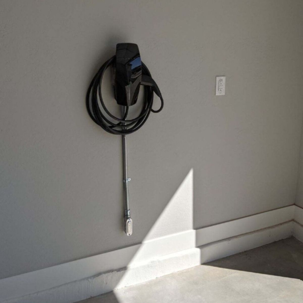 Wall-mounted EV charger with coiled cable on a gray garage wall, lit by sunlight