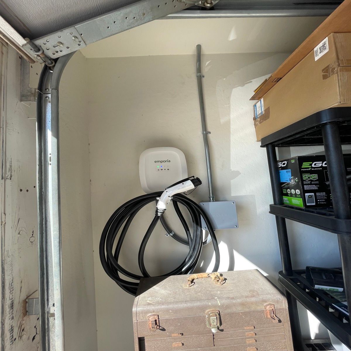 Garage interior with coiled black cable on wall, white device, shelving, and cardboard boxes.