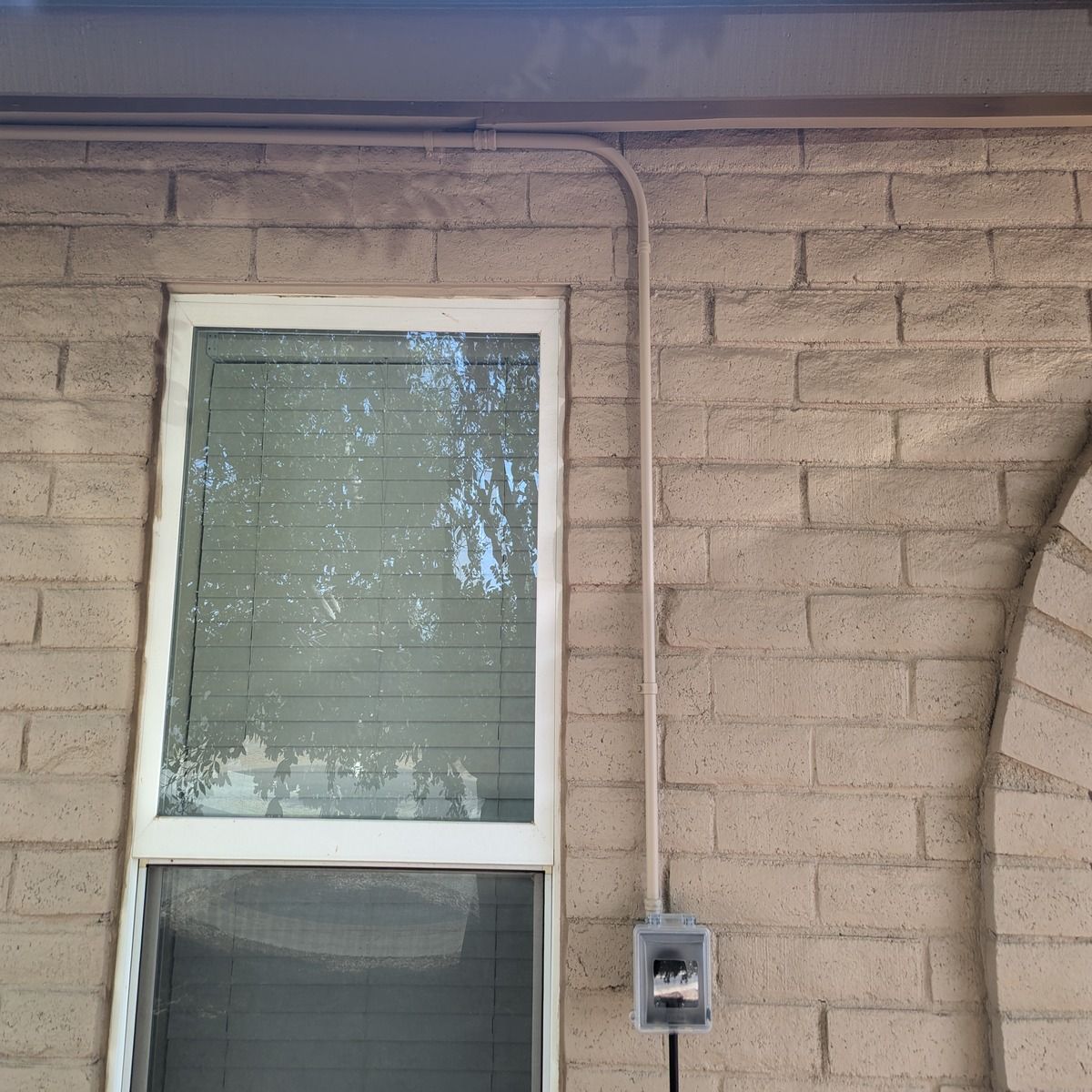 Exterior wall with a window, electrical conduit, and meter box on tan brick siding.