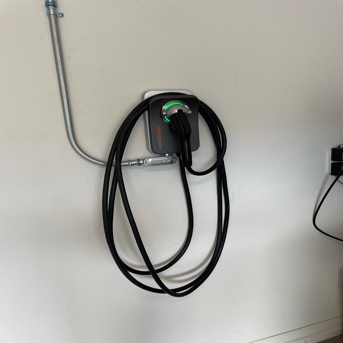 Wall-mounted EV charging cable coiled beside a metal conduit on a beige wall.