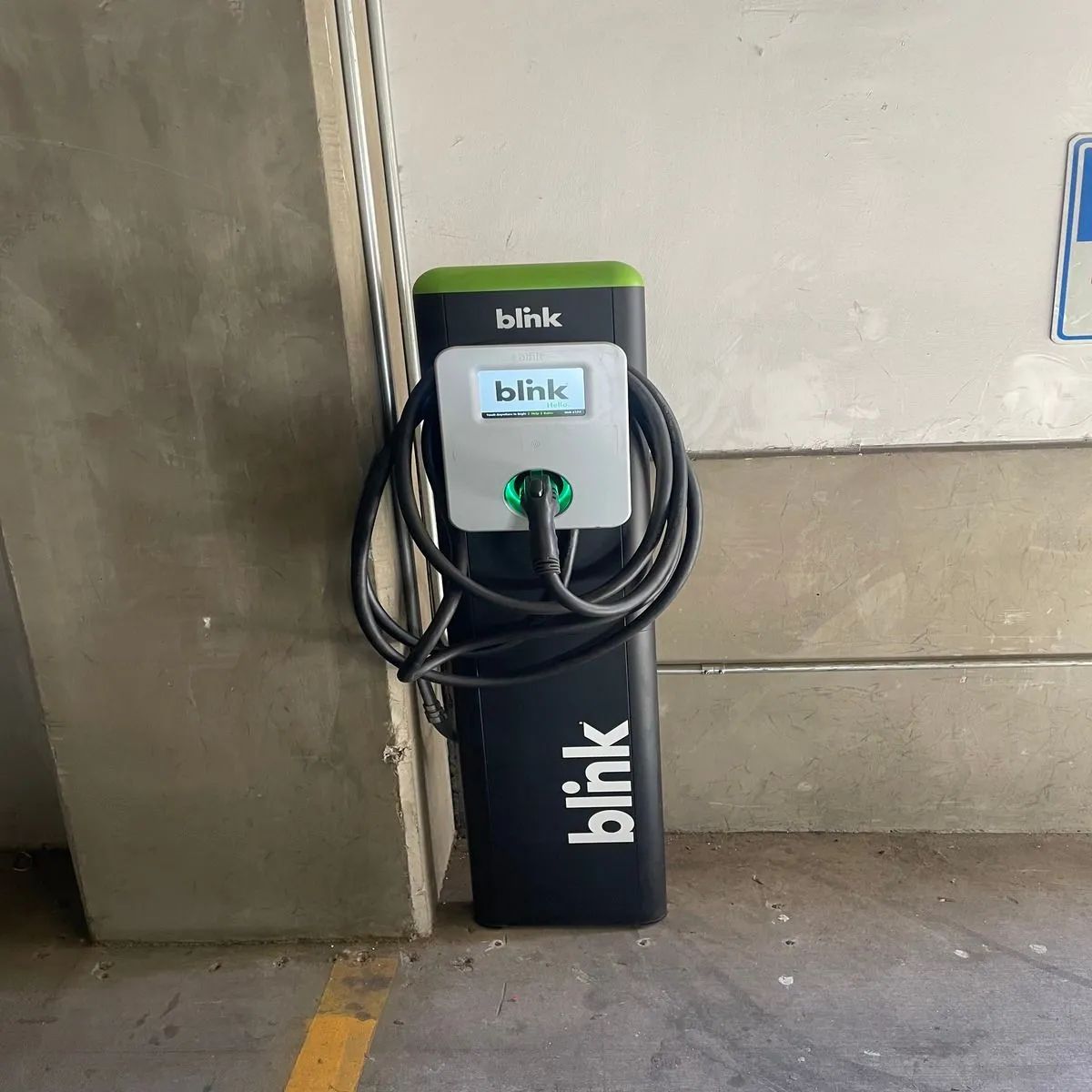 Blink charging station with coiled cable against a wall in a concrete parking area