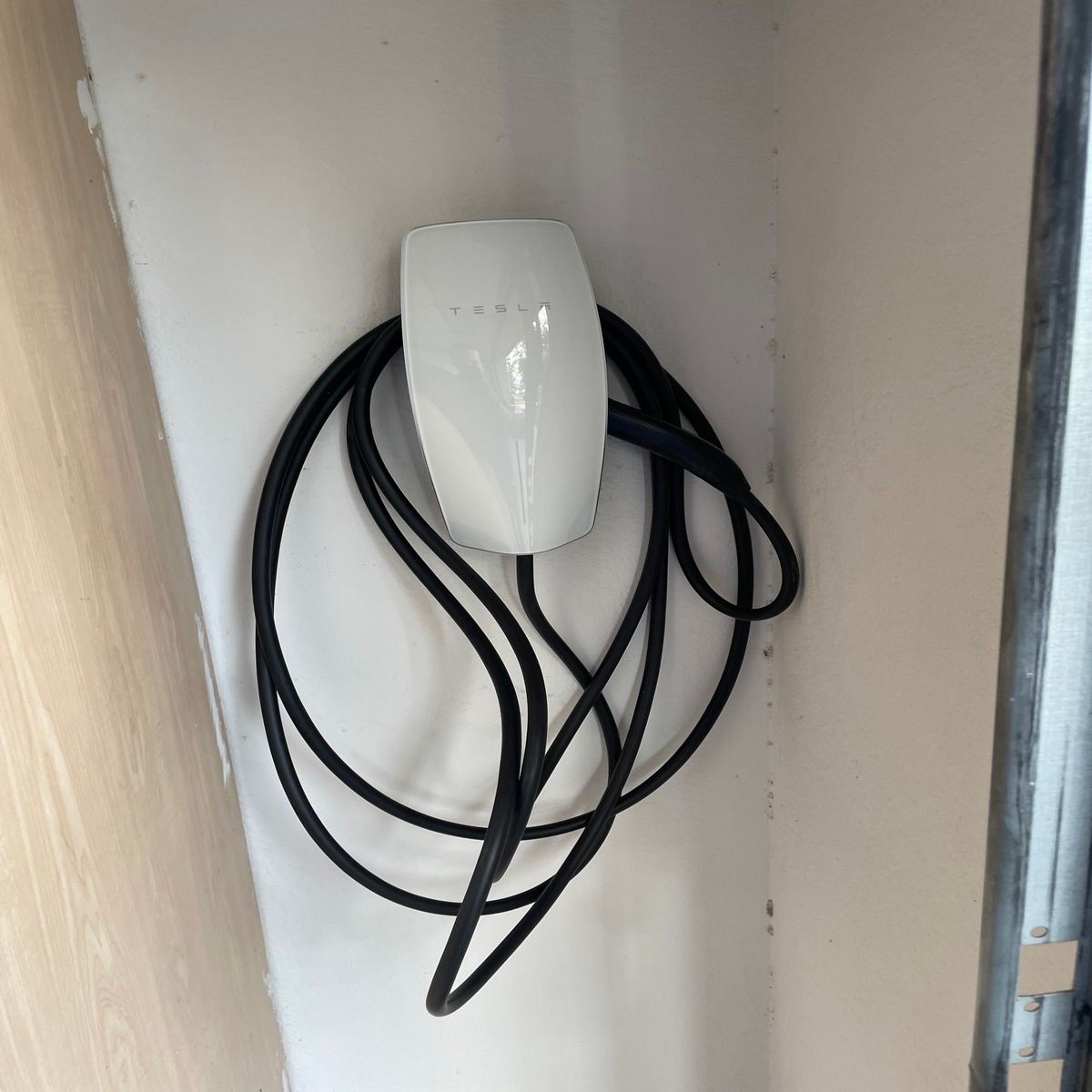 White wall-mounted device with a black coiled cable hanging beneath it in a small alcove.
