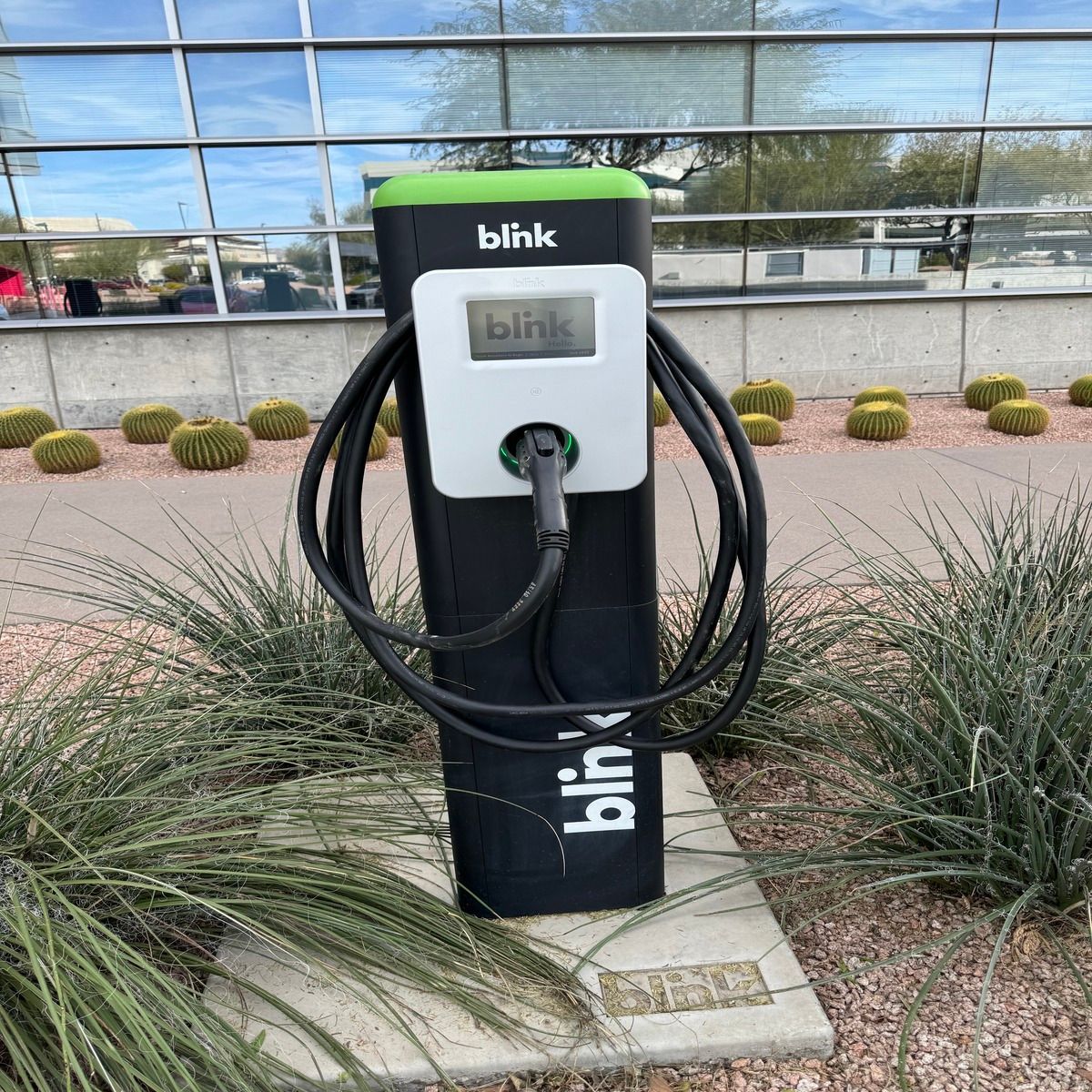 Blink EV charging station with coiled cable outside a glass-fronted building.