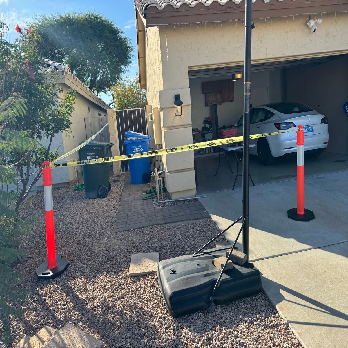 Driveway blocked by caution tape and orange cones in front of a garage with a car inside.
