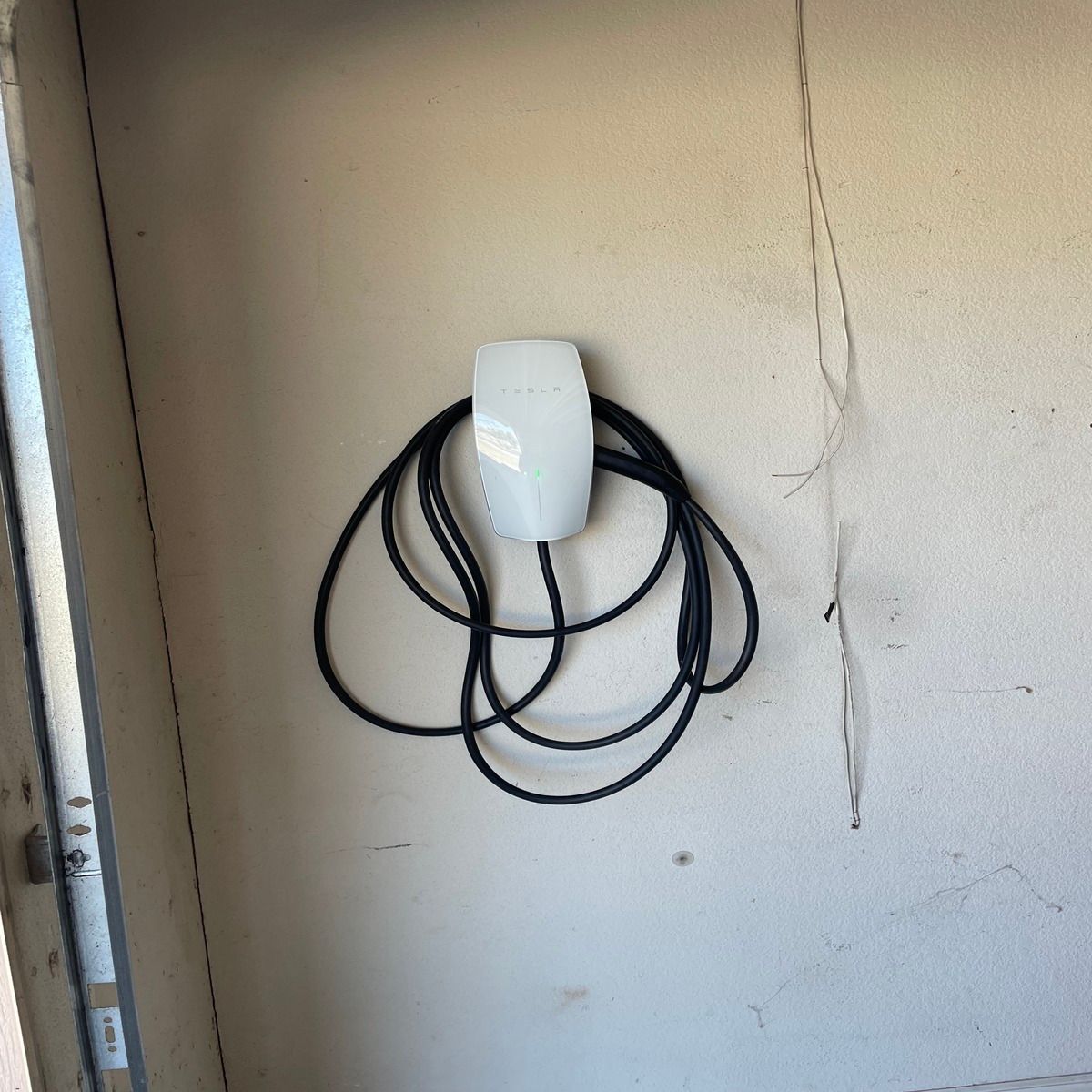 Coiled black cable hanging on a white wall-mounted device with a visible crack in the wall