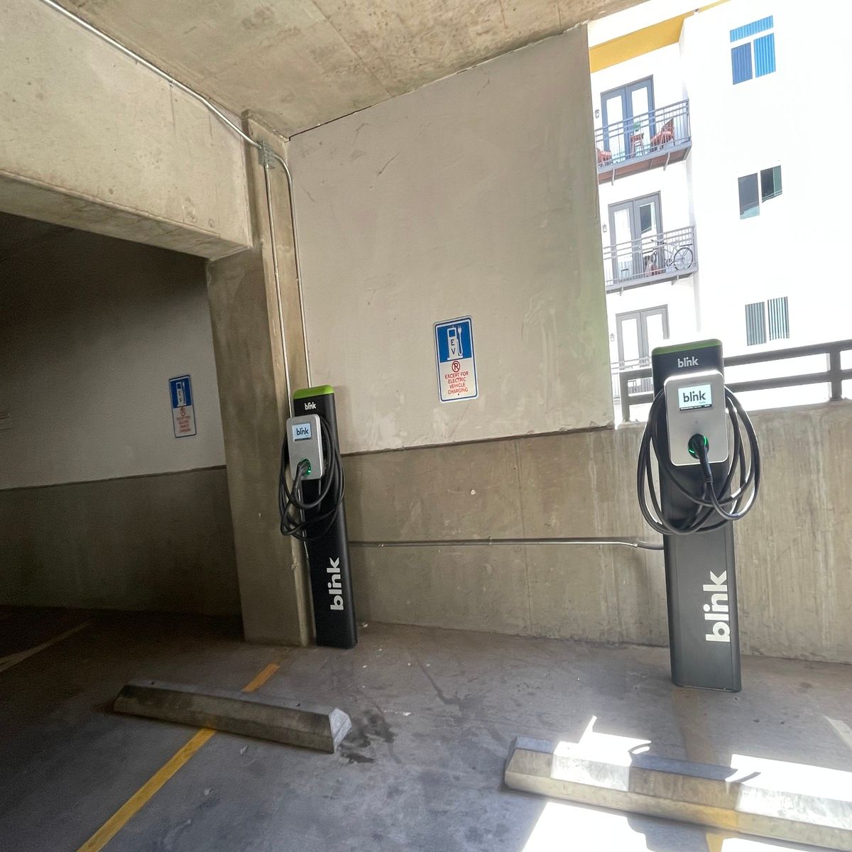 Two black Blink EV charging stations under a concrete overhang in an apartment parking area