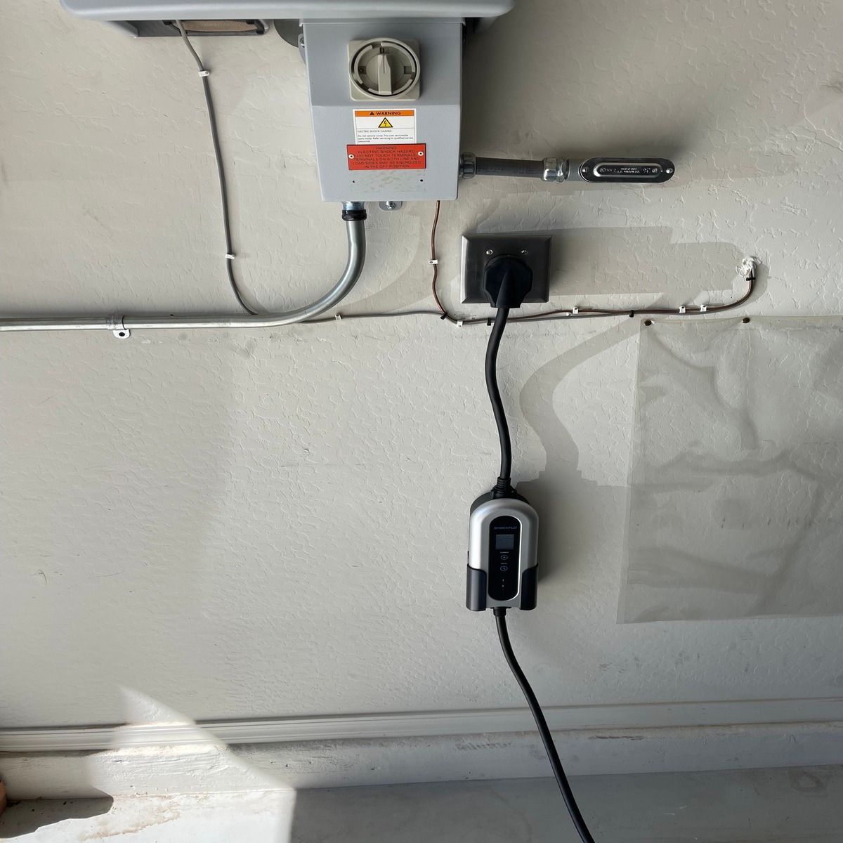 Wall-mounted electrical boxes and a plugged-in device with cables in a garage-like interior.