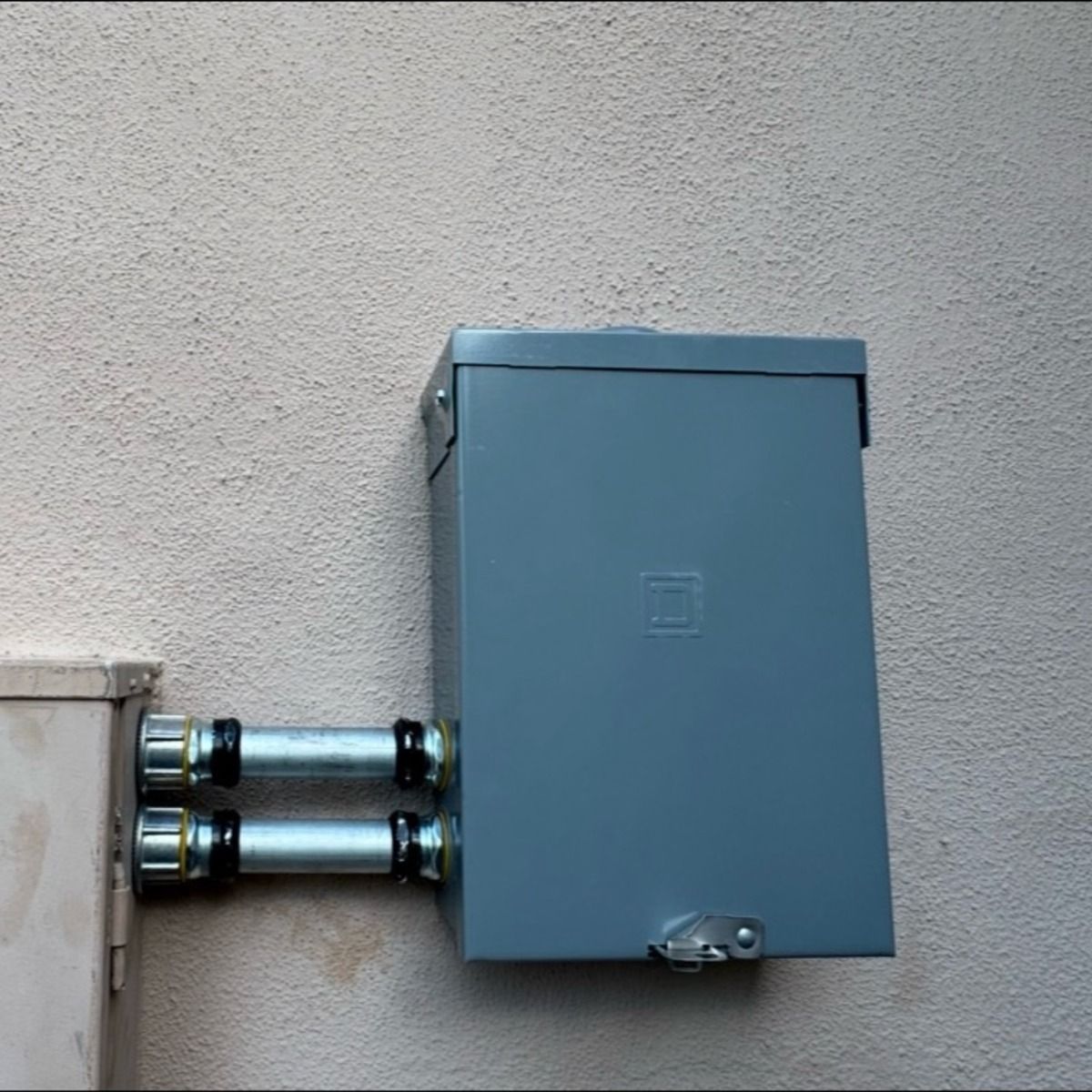 Gray electrical box with conduit pipes mounted on a stucco wall