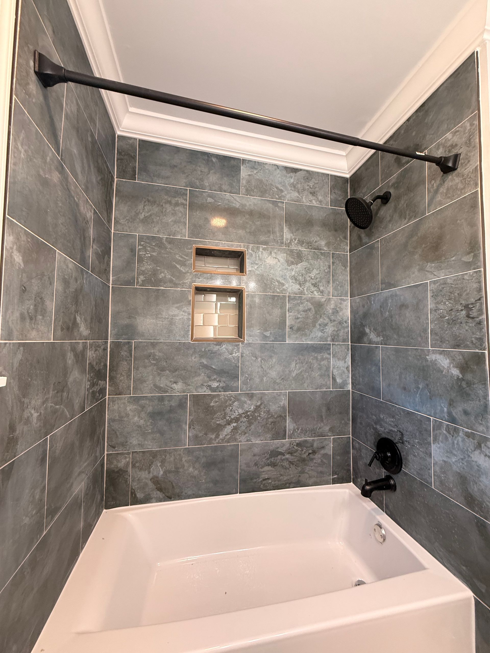 Modern tiled bathtub shower with black fixtures and a small recessed shelf