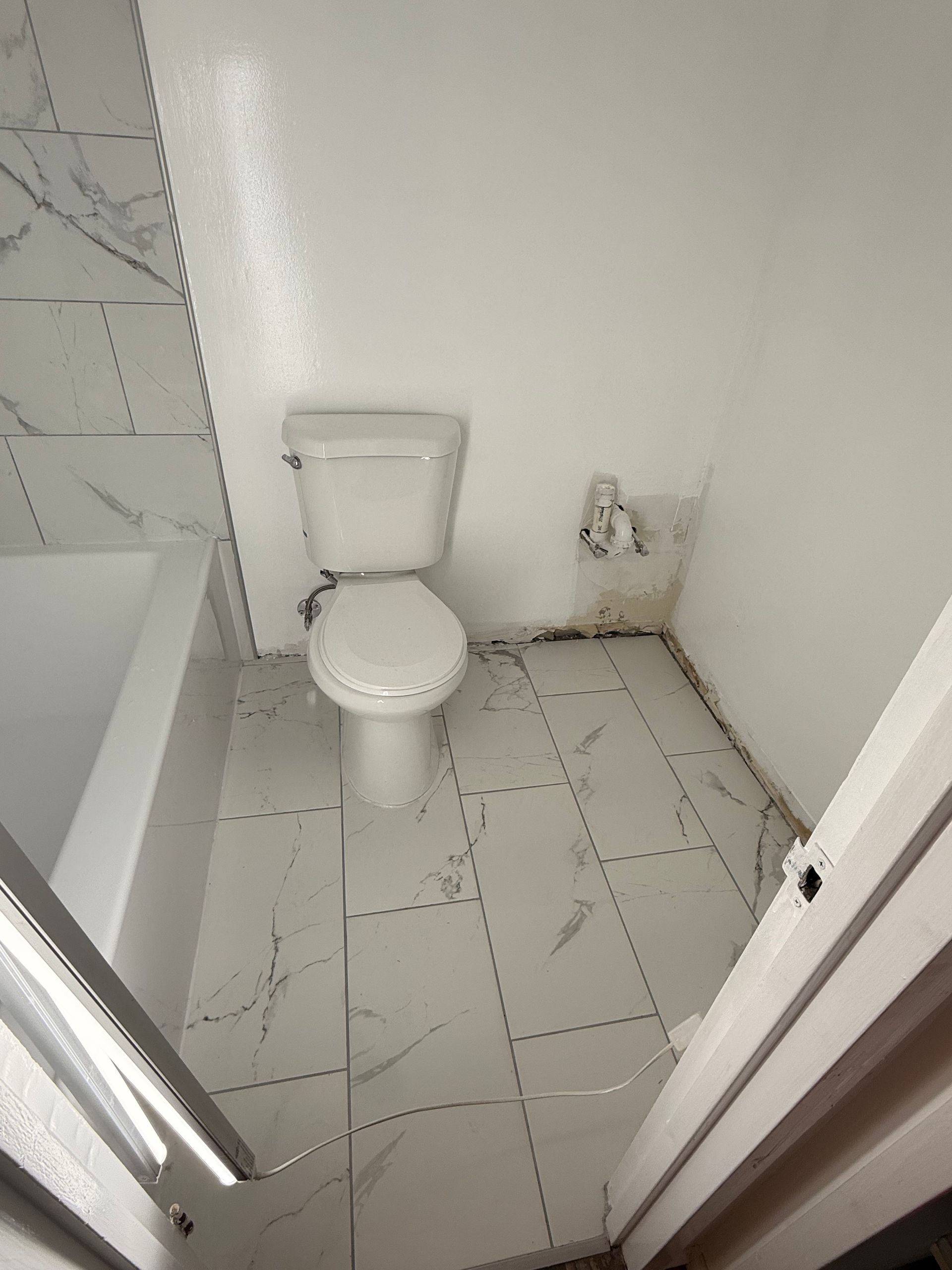 Small bathroom with a toilet, white walls, tiled floor, and a bathtub edge visible on the left.