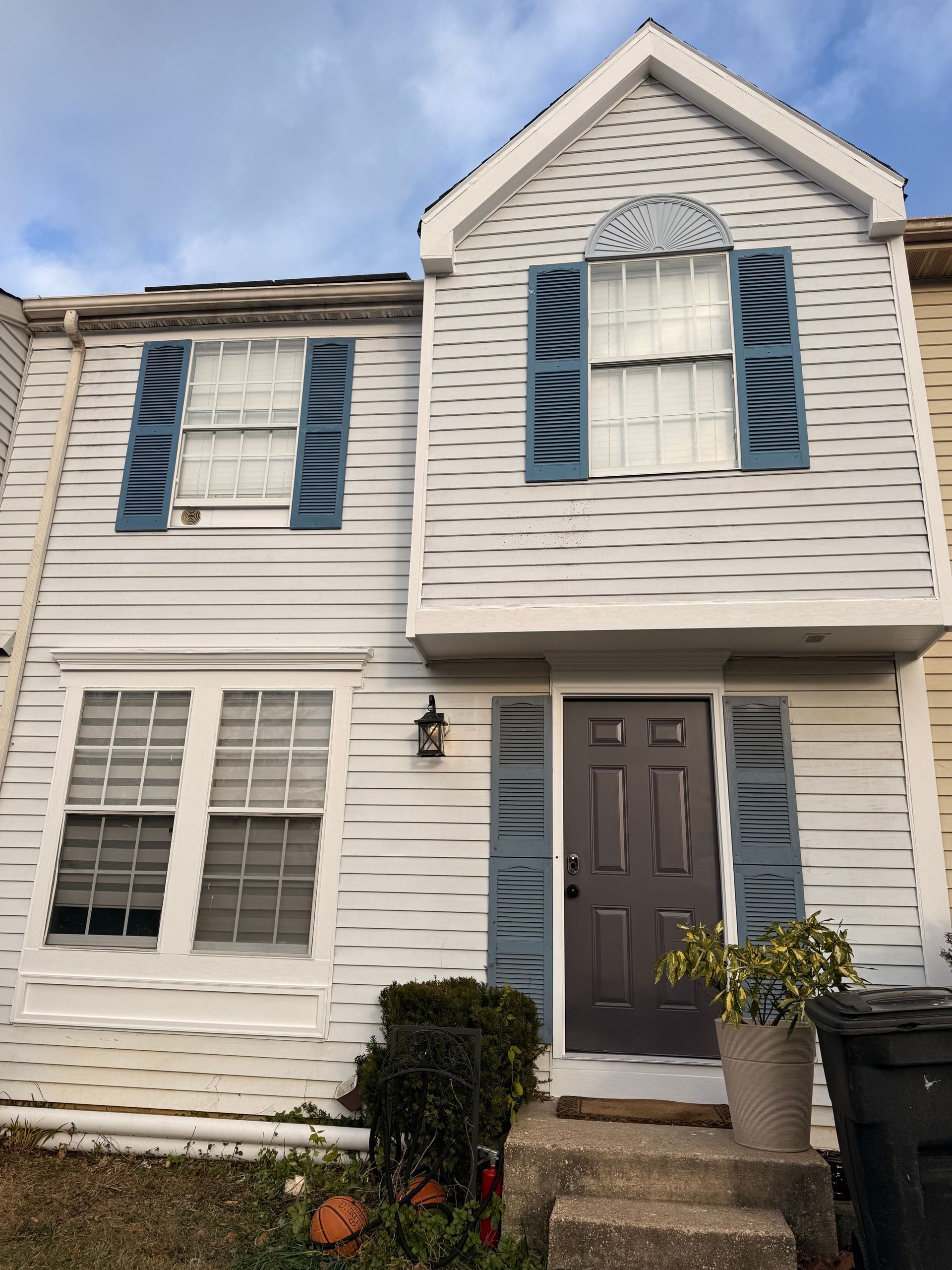 White townhouse with blue shutters, gray door, and small front shrubs under a cloudy sky