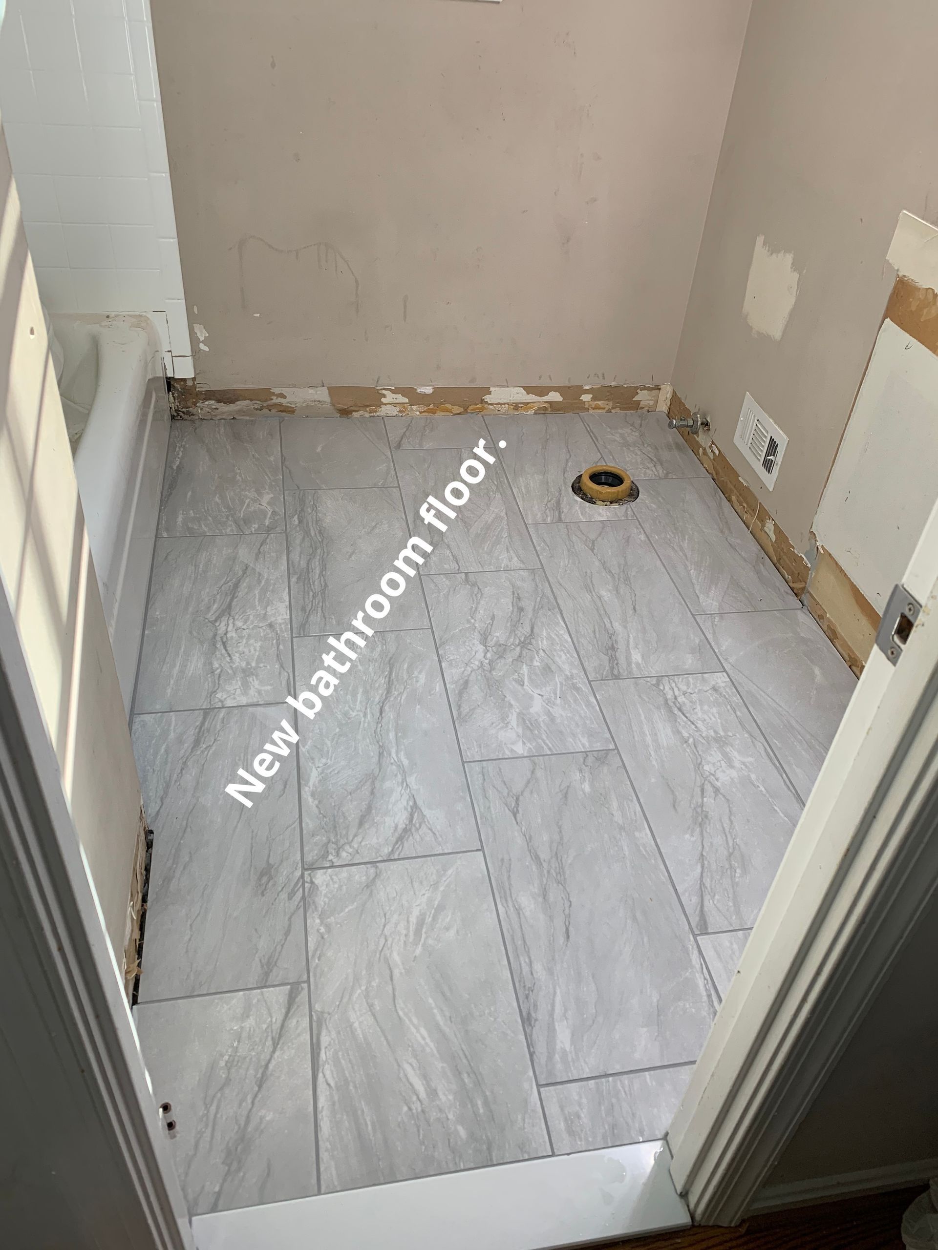 Small bathroom with new gray tile floor, unfinished walls, and a drain near the back wall.