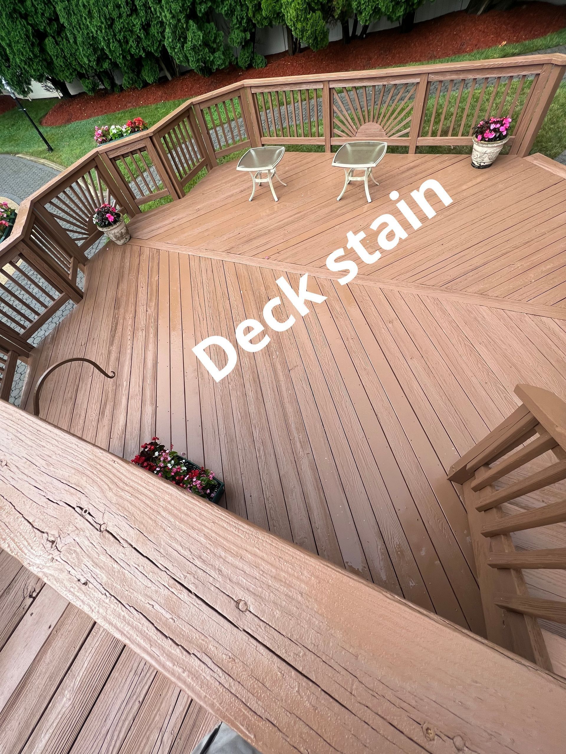 Wooden deck with visible stain marks, railing, chairs, and potted flowers
