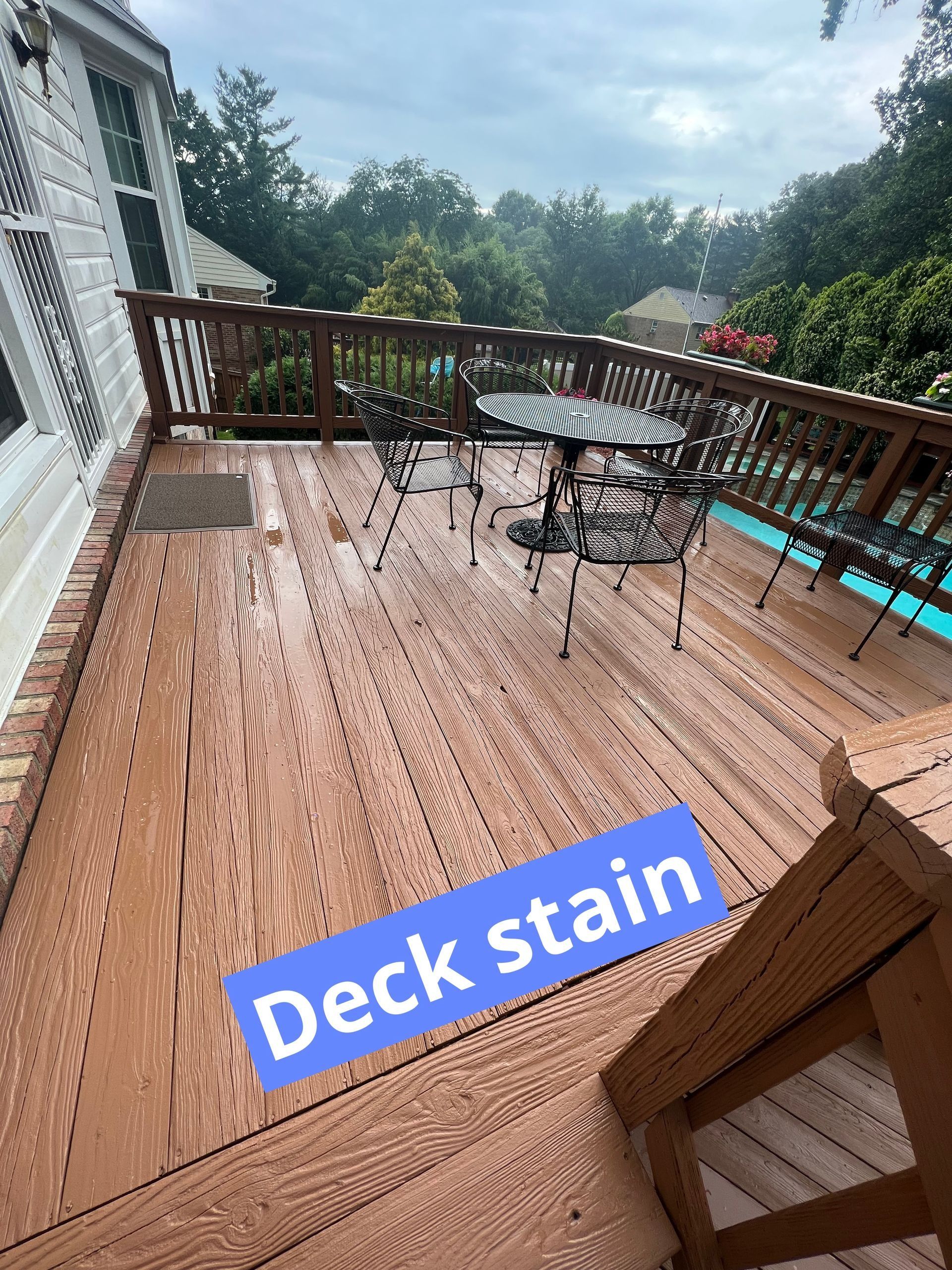 Rain-soaked wooden deck with railing, patio table, chairs, and “Deck stain” text overlay