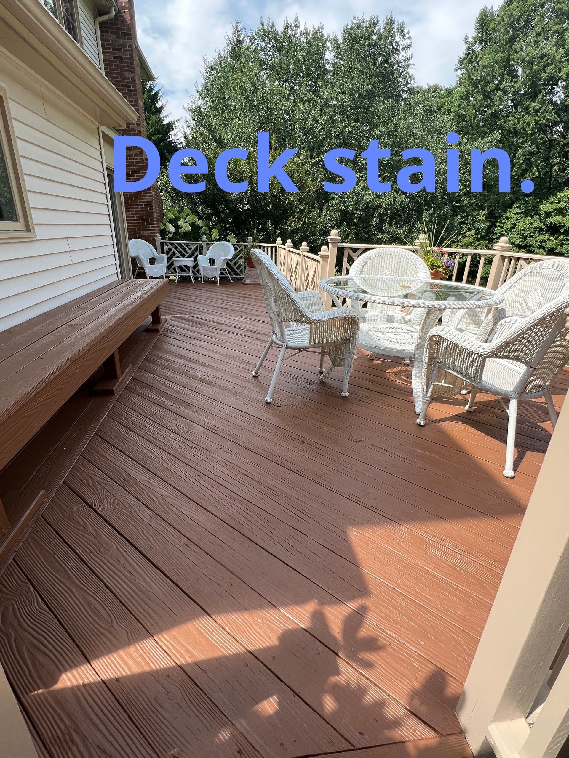 Wooden deck with fresh stain, white patio chairs, and a house exterior in sunlight.