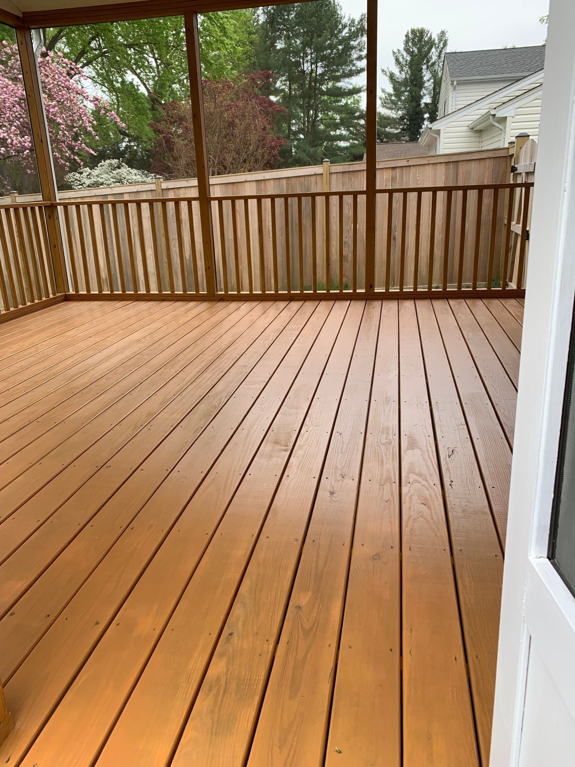 Wooden backyard deck with railings and a view of trees and neighboring houses
