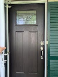 Front door with a small window, silver handle, and green siding on the right.